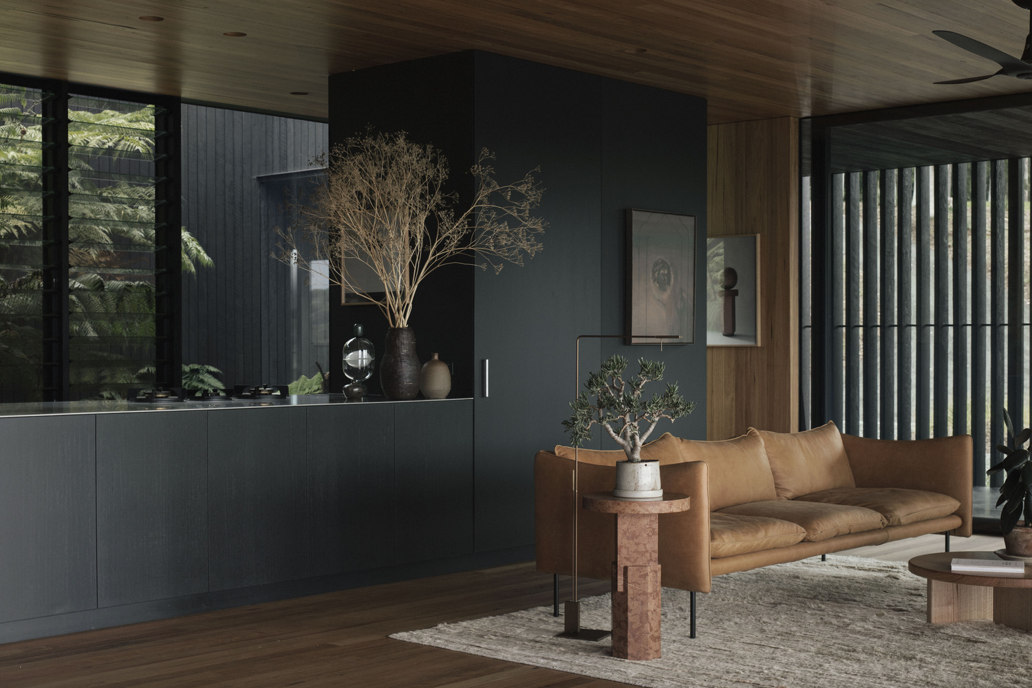 Sofa phòng khách lựa chọn vật liệu da lộn màu nâu hài hòa với trần và sàn gỗ xung quanh. Bên cạnh là chậu cảnh bonsai nghệ thuật theo phong cách Nhật Bản.