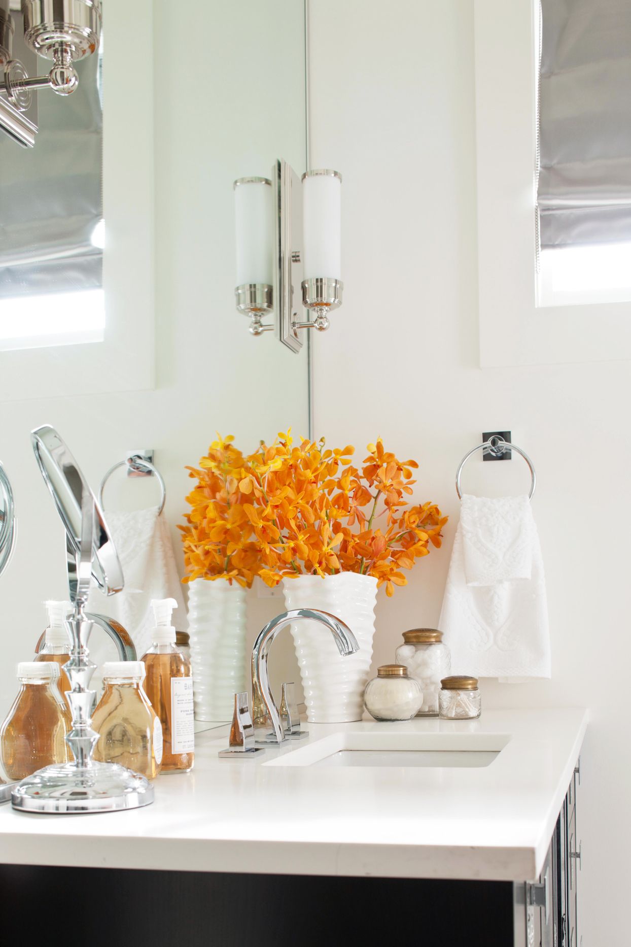 Dành thời gian sắp xếp lại khu vực bồn rửa và thêm vào những điểm nhấn màu sắc như hoa tươi màu cam giữa căn phòng toàn sắc trắng sẽ làm góc nhỏ bừng sáng lên.
