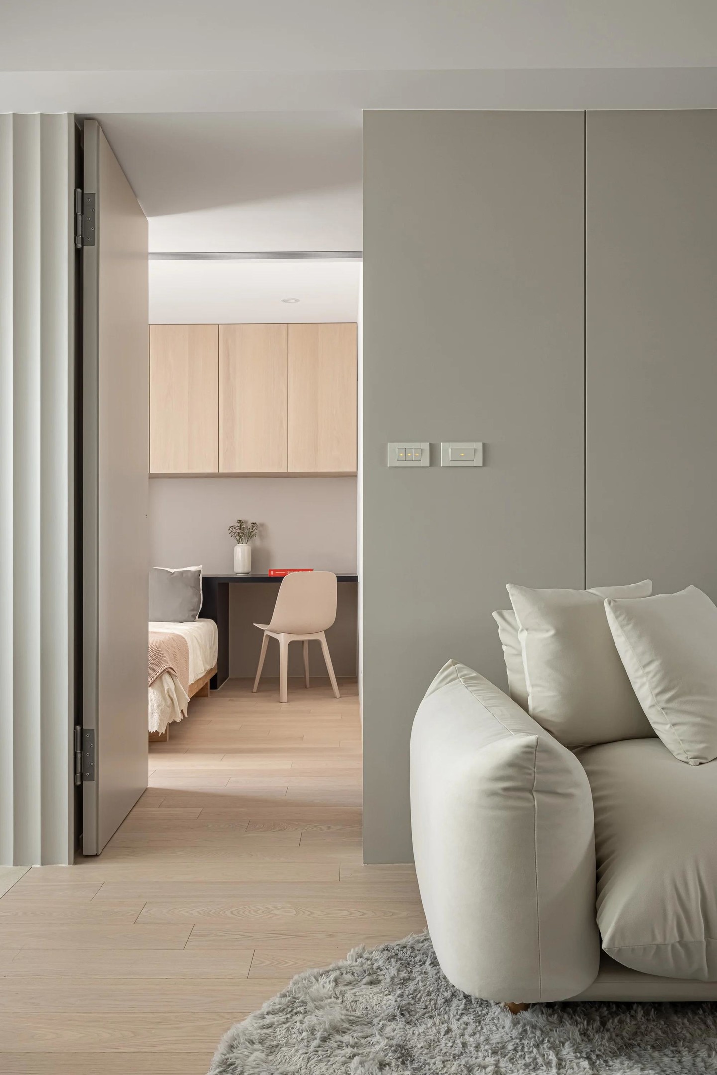 Phòng ngủ được thiết kế riêng biệt để tạo sự riêng tư, bố trí ngay phía sau sofa phòng khách. Sàn gỗ xuyên suốt không gian, kết hợp hệ thống tủ lưu trữ sát trần phía trên bức tường phòng ngủ nhằm tối ưu hóa không gian.
