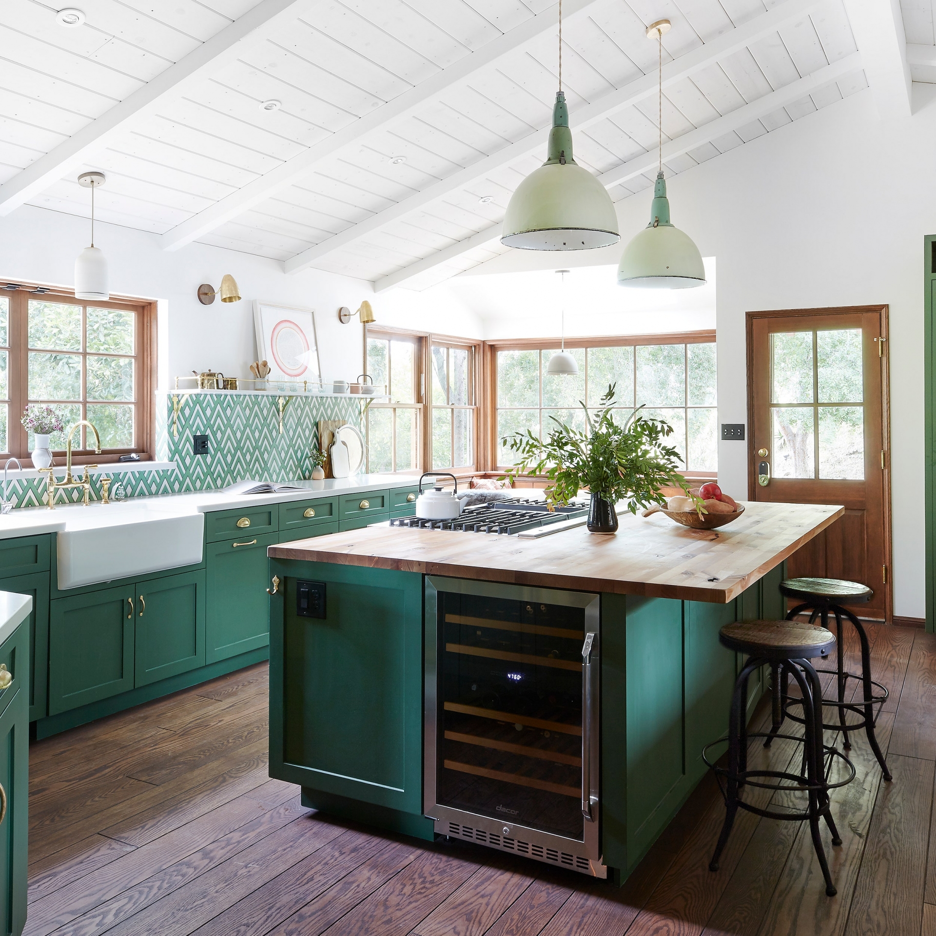 Phòng bếp sử dụng gam màu xanh ngọc lục bảo để sơn tủ lưu trữ và đảo bếp. Vẻ đẹp sang trọng của gam màu này kết hợp với màu nâu tự nhiên của gỗ cùng những ô cửa sổ đầy nắng cho vẻ đẹp vừa sang trọng vừa ấm áp.