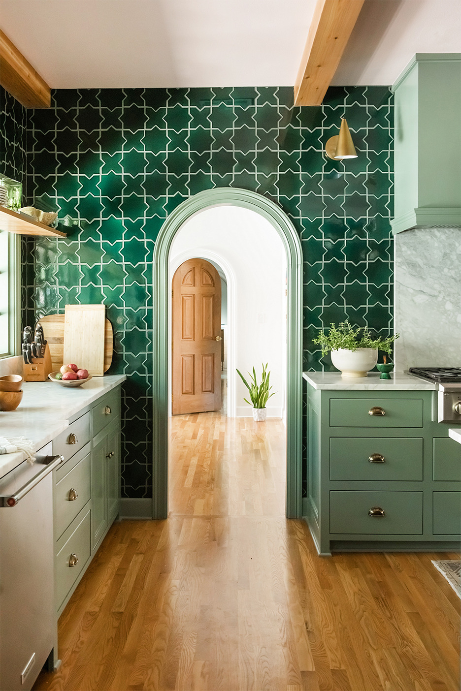 Phòng bếp thiết kế theo phong cách cổ điển với mái vòm cong mềm mại ở cửa chuyển tiếp. Gạch màu xanh ngọc lục bảo được ốp xung quanh bức tường này, kết hợp với hệ tủ bếp màu xanh bạc hà và sàn gỗ cho cái nhìn hài hòa.