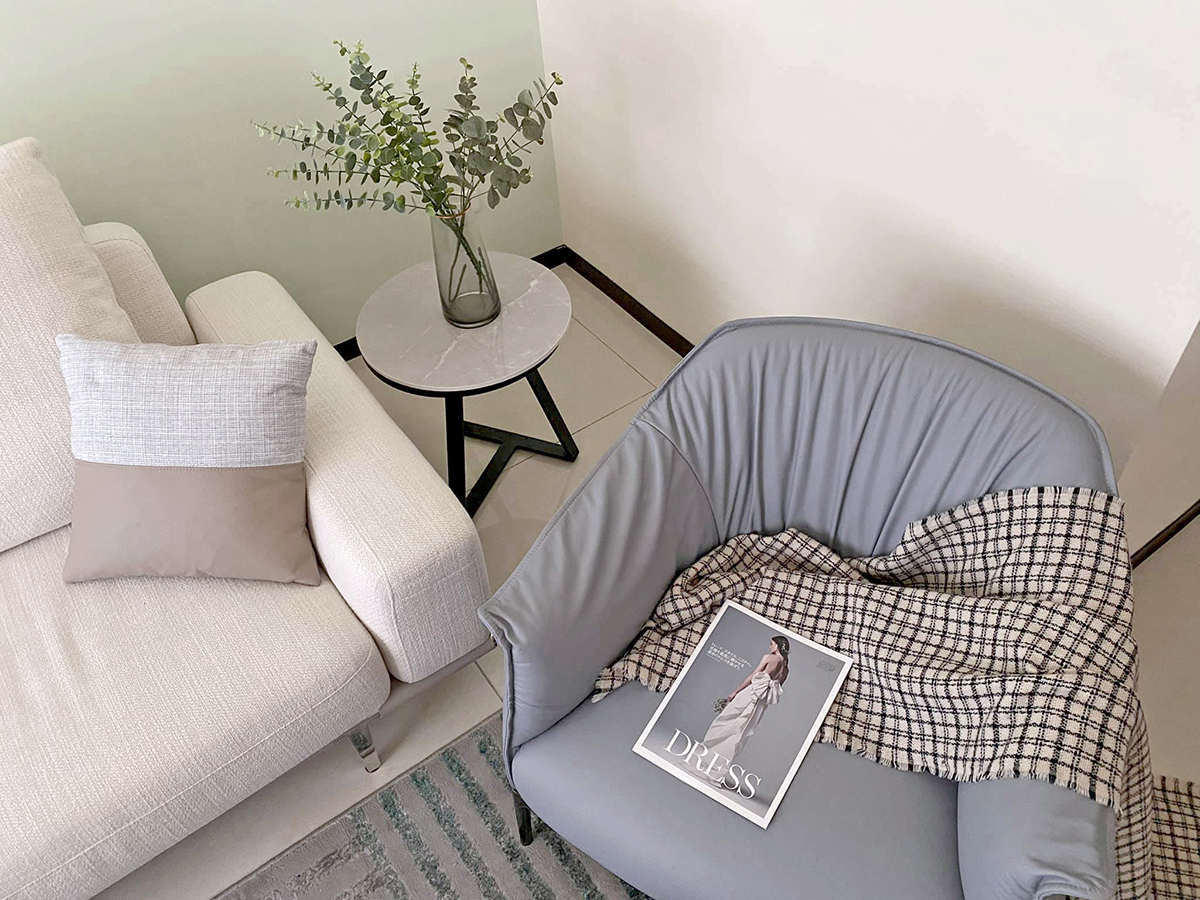 Ghế sofa góc màu trắng tươi sáng được thiết kế theo kiểu module linh hoạt, bên cạnh là chiếc ghế bành màu xam lam và bàn phụ để trang trí lọ hoa xinh xắn.
