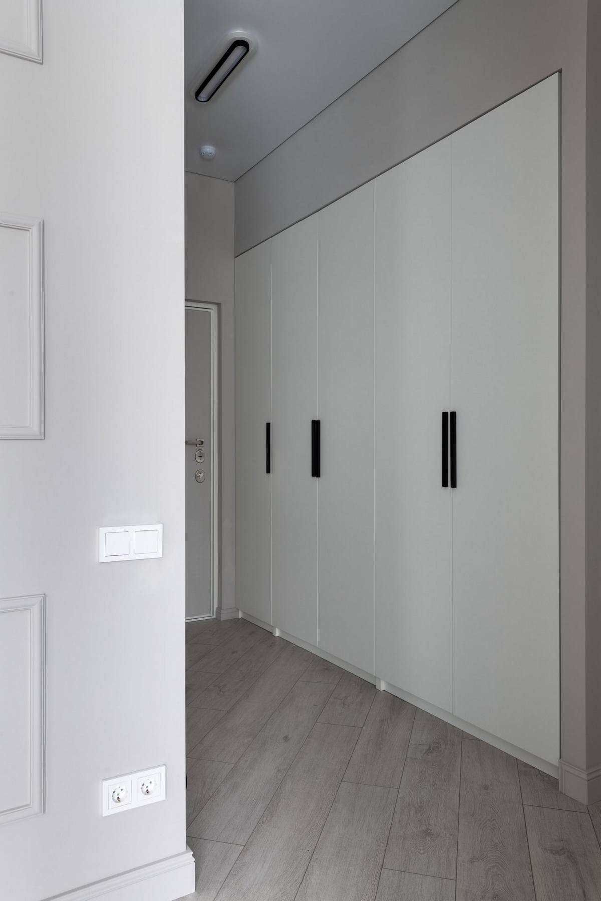 Lối vào đơn giản với sàn nhà lát gỗ dẫn lối vào khu vực sinh hoạt bên trong. Hệ thống tủ lưu trữ âm tường màu trắng giúp khu vực này luôn gọn gàng, ngăn nắp.