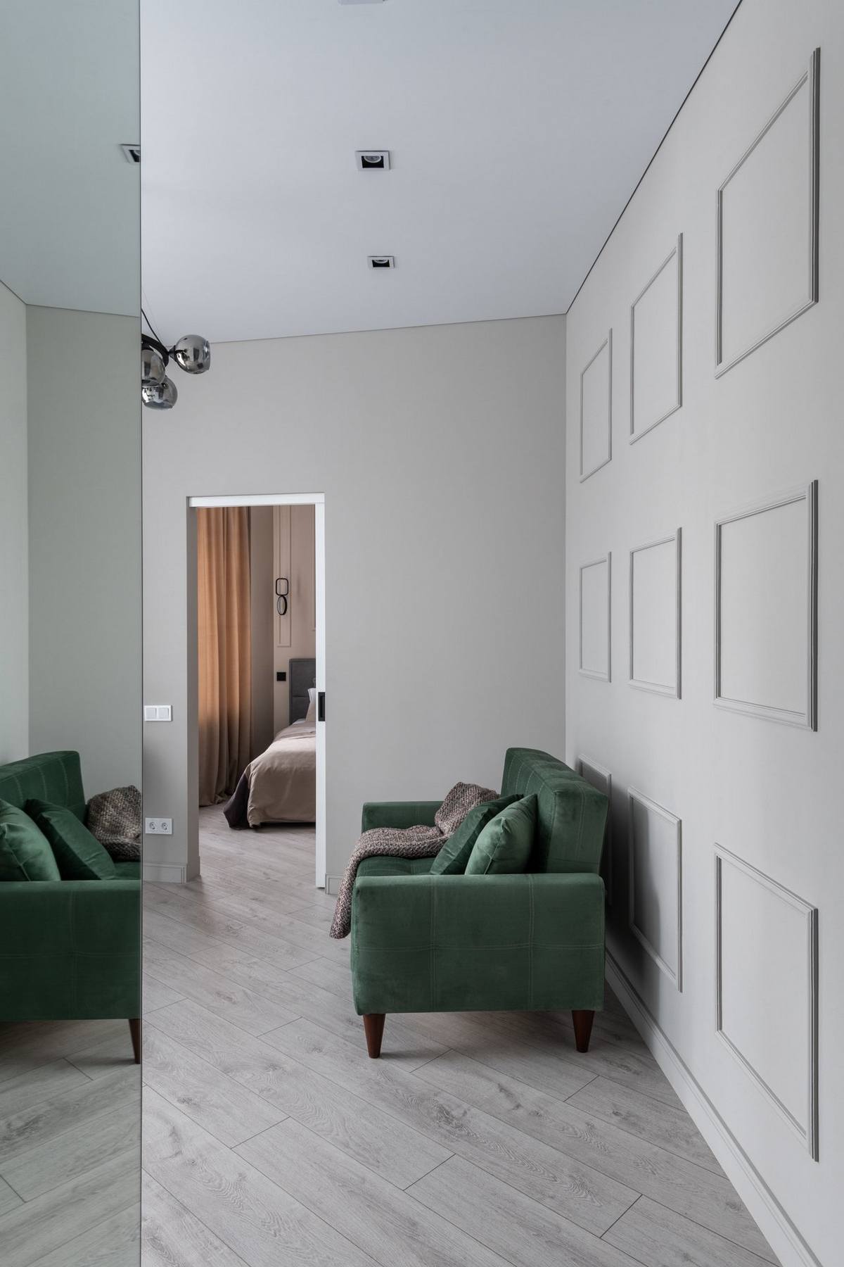 Một chiếc ghế sofa màu xanh ngọc lục bảo được bố trí sát tường, phía sau là phào chỉ hình vuông tối giản thay thế cho tranh treo tường quen thuộc.