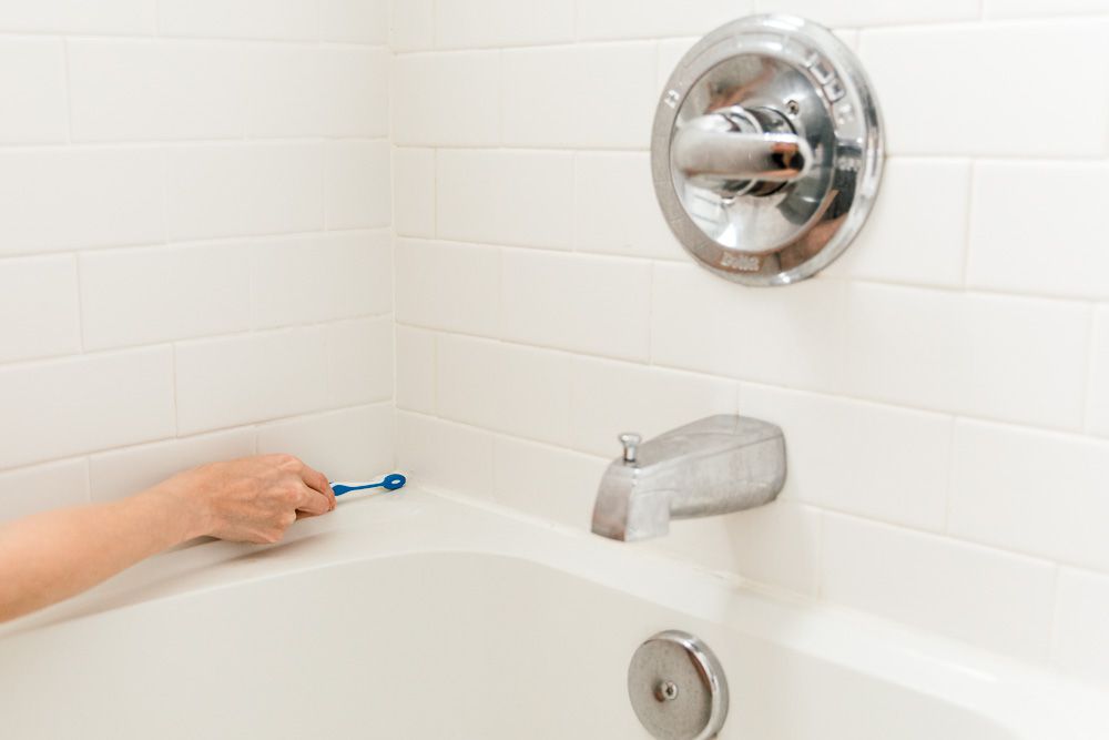 Xử lý váng xà phòng bằng bàn chải đánh răng cũ, bắt đầu cọ rửa các góc nơi bồn tắm tiếp xúc với tường. 