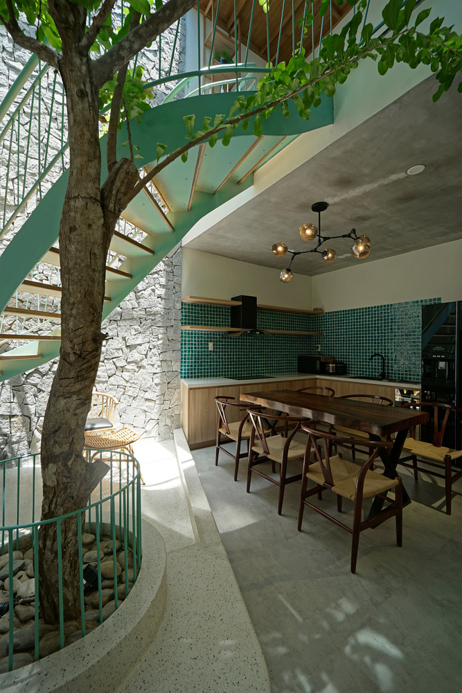 Phòng bếp thiết kế kiểu chữ L với tường ốp gạch mosaic màu xanh ngọc lục bảo nổi bật, tương phản với tone màu gỗ trầm ấm của bộ bàn ghế ở khu vực ăn uống liền kề.