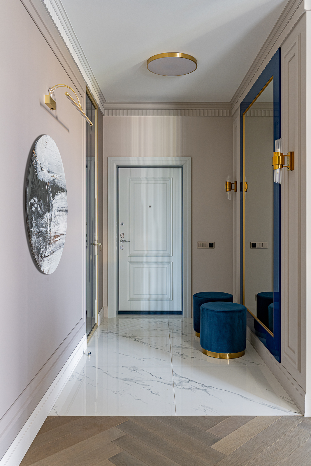 Lối vào căn hộ lát đá cẩm thạch cùng chiếc ghế đôn và tấm gương cỡ lớn viền khung màu xanh lam đậm, kết hợp các chi tiết mạ vàng đồng sang chảnh.