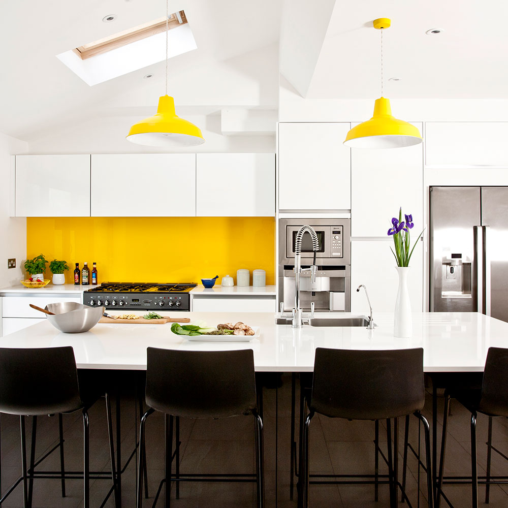 NTK đã sử dụng màu vàng để kết nối backsplash phòng bếp với đèn thả trần ở bàn ăn. Bộ ghế ngồi màu đen cũng tăng cảm giác mạnh mẽ, vững chãi cho khu vực này.