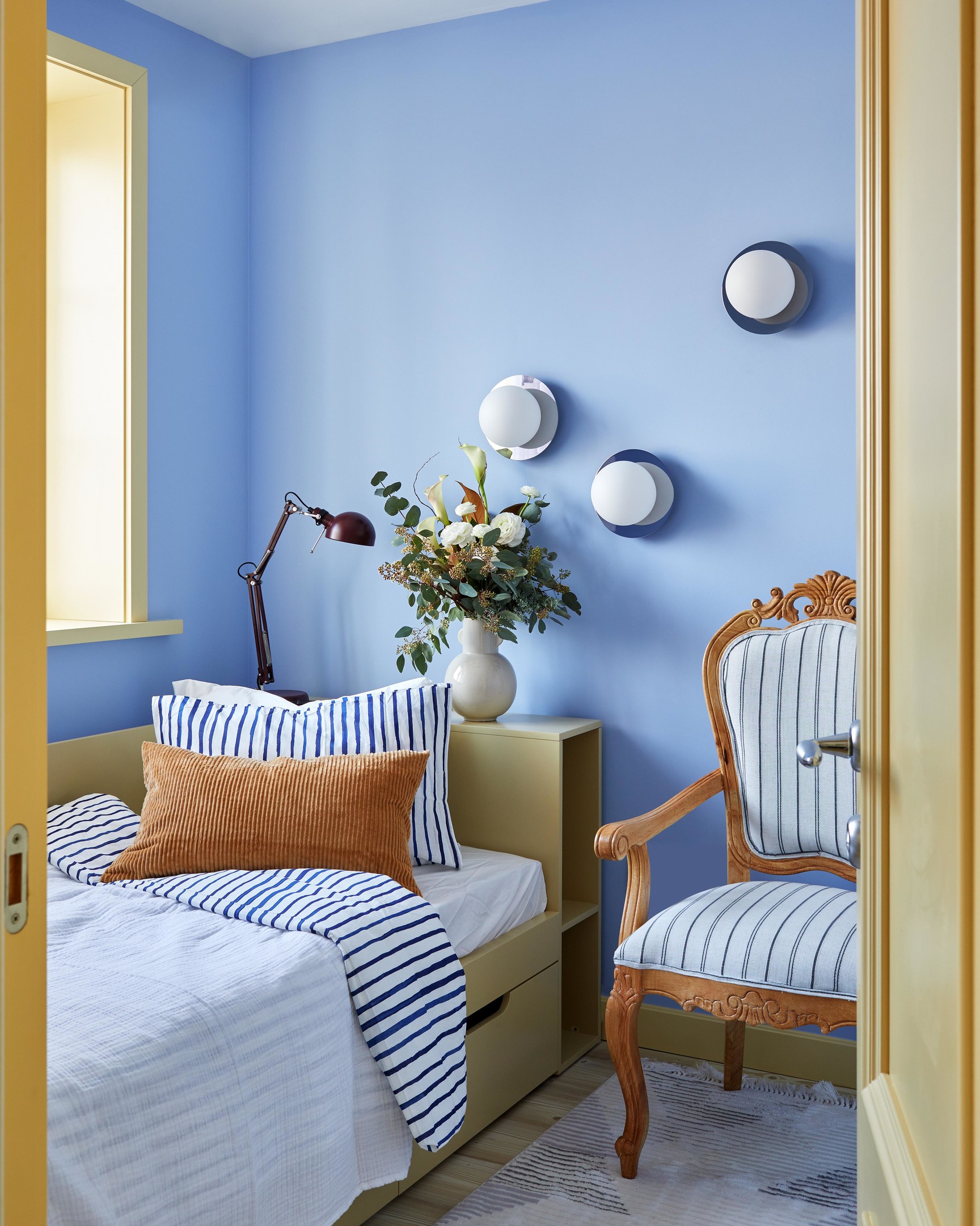 Phòng ngủ siêu nhỏ nhưng siêu xinh với sơn tường màu xanh lam dịu mát cùng họa tiết kẻ sọc phong cách Địa Trung Hải. Bên cạnh đèn bàn, bộ ba đèn gắn tường hình quả cầu vừa cung cấp ánh sáng vừa trang trí cho bức tường bắt mắt.