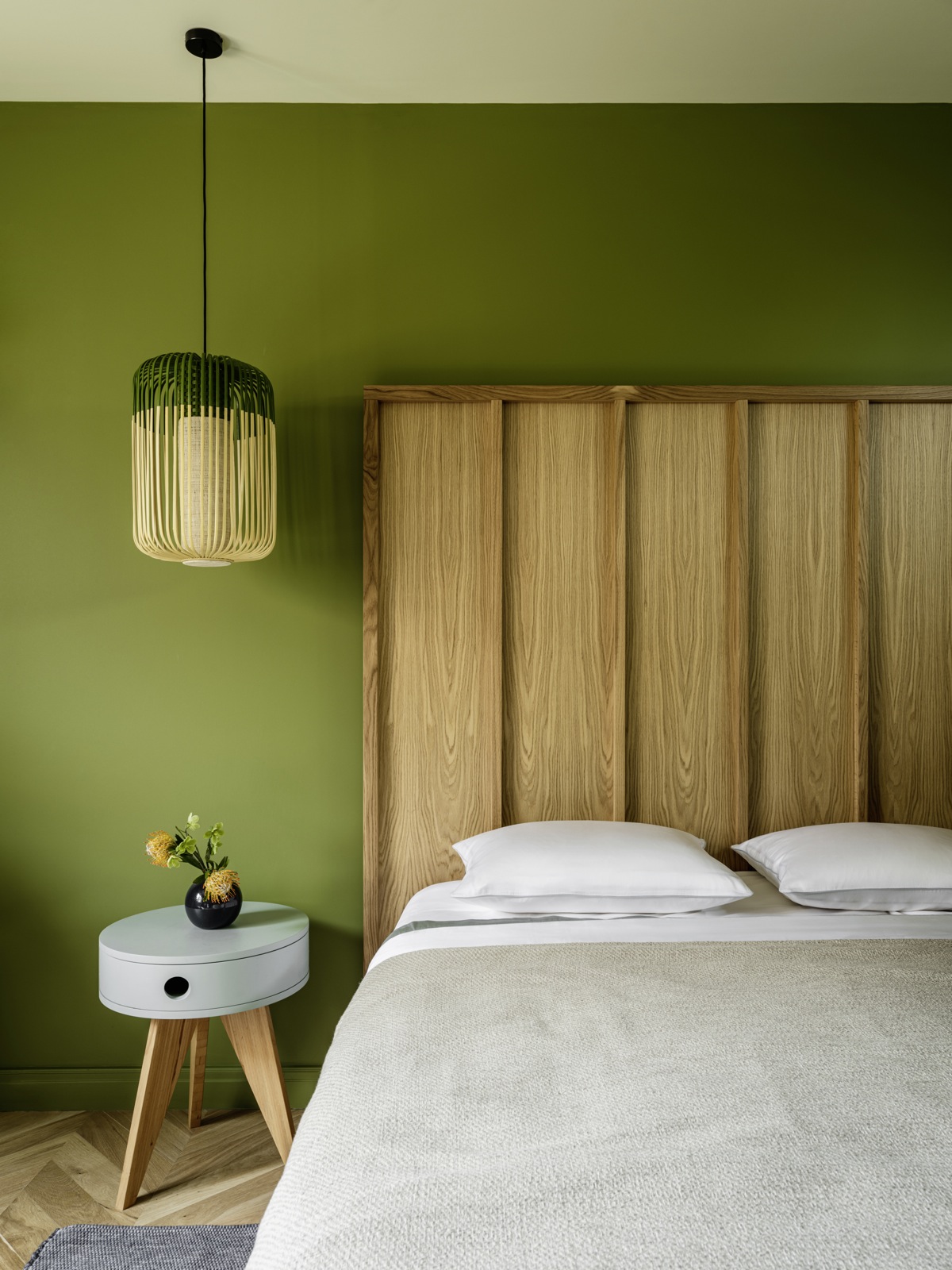 Vẻ đẹp mướt xanh và gần gũi với thiên nhiên nhờ gam màu xanh lá cây đậm nhạt cùng nội thất gỗ khiến ai bước vào phòng ngủ này cũng thấy thoải mái. Đặc biệt phải kể đến chiếc đèn thả trần “tone sur tone” duyên dáng với nền tường.
