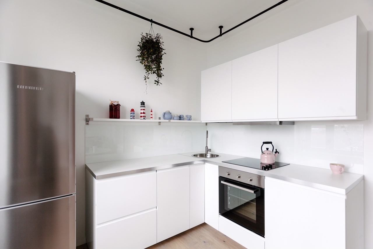 Phòng bếp thiết kế kiểu chữ L với gam màu trắng chủ đạo, kết hợp cả tủ kín và kệ mở để tăng không gian lưu trữ, riêng tủ lạnh làm bằng thép không gỉ bề mặt sáng bóng bắt mắt.