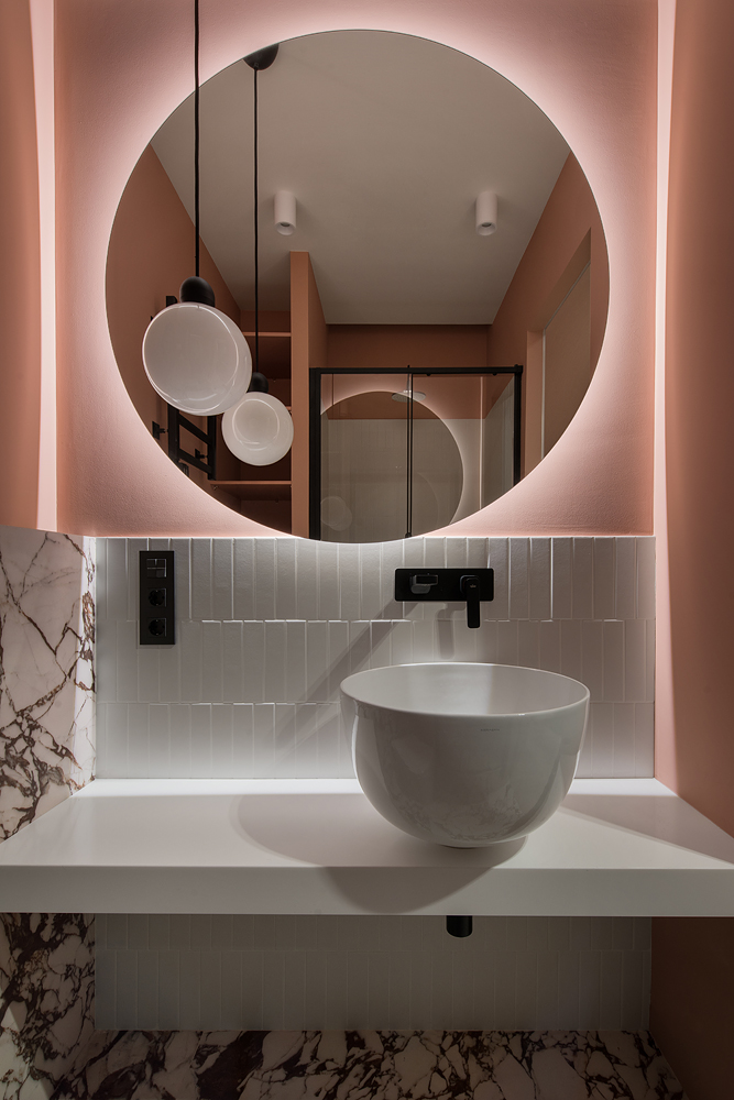 Một mẹo nhỏ để tăng sự ấm cúng cho phòng tắm chính là kết hợp giữa màu sắc (ở đây là hồng pastel) và ánh sáng như đèn từ gương soi và đèn thả trần này chẳng hạn.
