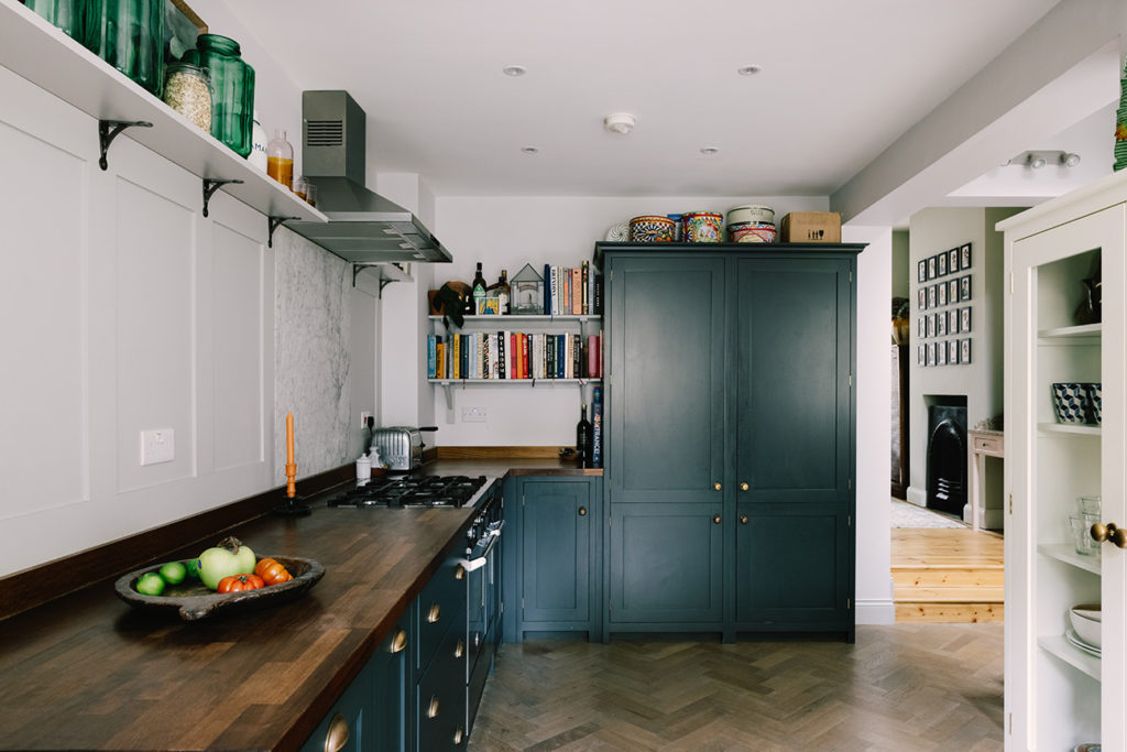 Phòng bếp thiết kế kiểu chữ L với tủ truyền thống sơn màu xanh cổ vịt cùng tay nắm cửa mạ vàng đồng, đồng thời kết hợp các dãy kệ mở lưu trữ ở cả 2 góc tường.