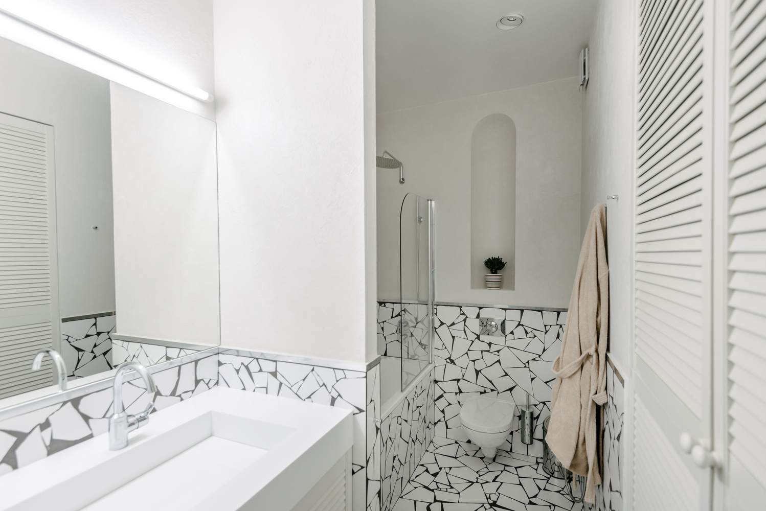Gạch ốp tường và lát sàn phòng tắm cùng loại với lối vào và phòng bếp, tạo sự kết nối giữa các khu vực chức năng. Toilet gắn tường giúp tiết kiệm diện tích, phân vùng với bồn tắm nằm bằng cửa gương trong suốt.