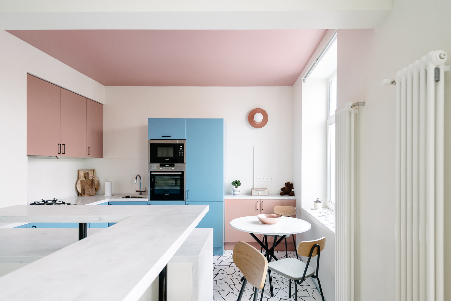 Các gam màu xanh lam và hồng phấn được sử dụng để làm nổi bật phòng bếp cũng như khu vực ăn uống. Đặc biệt, trần phòng bếp sơn hồng “tạo khối, tạo nét tương phản nhẹ nhàng với màu trắng chủ đạo của phòng khách và lối ra vào.