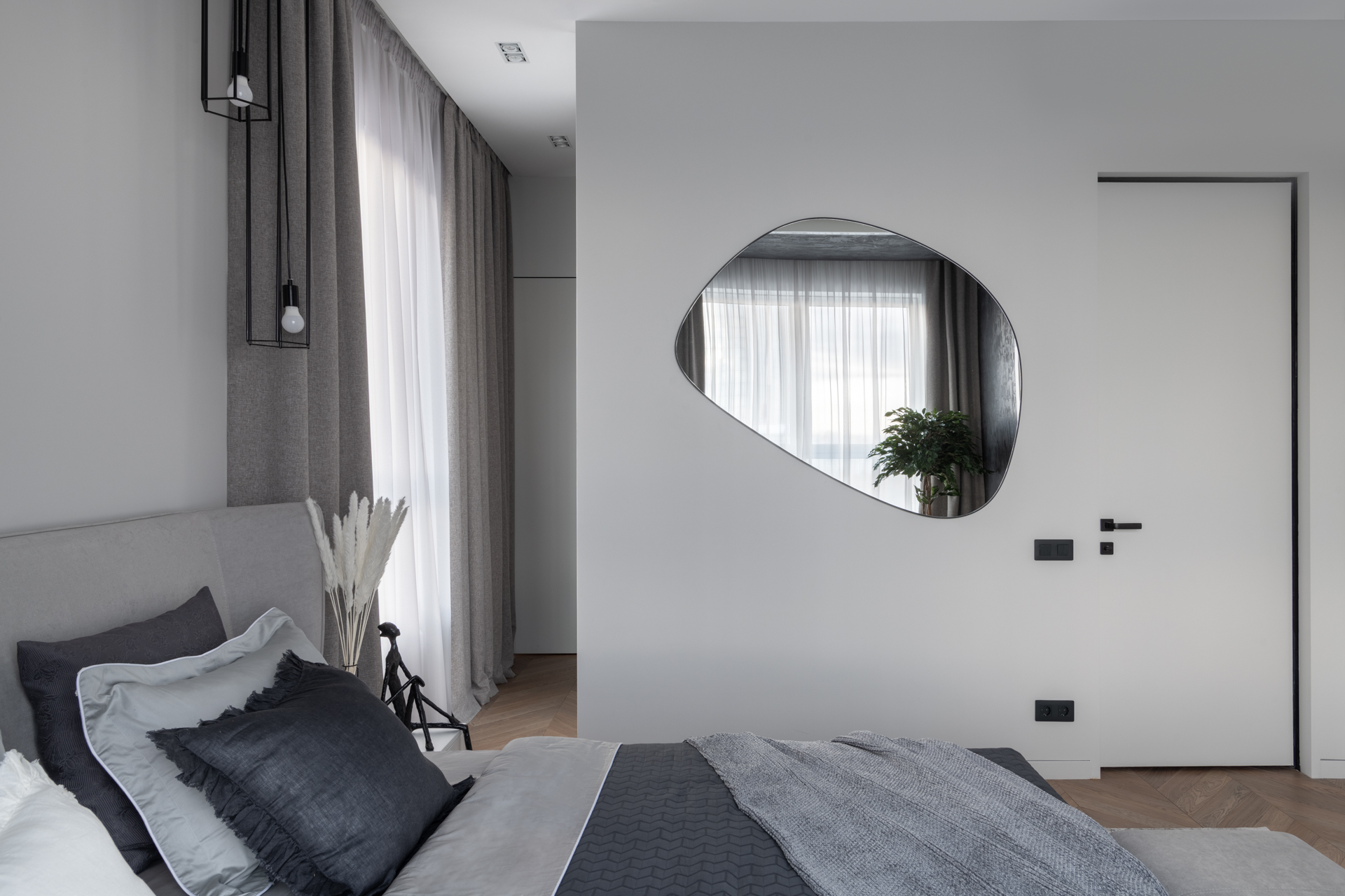 Phòng ngủ thiết kế tối giản nhưng gây ấn tượng nhờ tấm gương kiểu dáng đặc biệt, phản chiếu ô cửa sổ đầy nắng ấm cùng chậu cây cảnh để tăng thêm sắc xanh cho không gian.