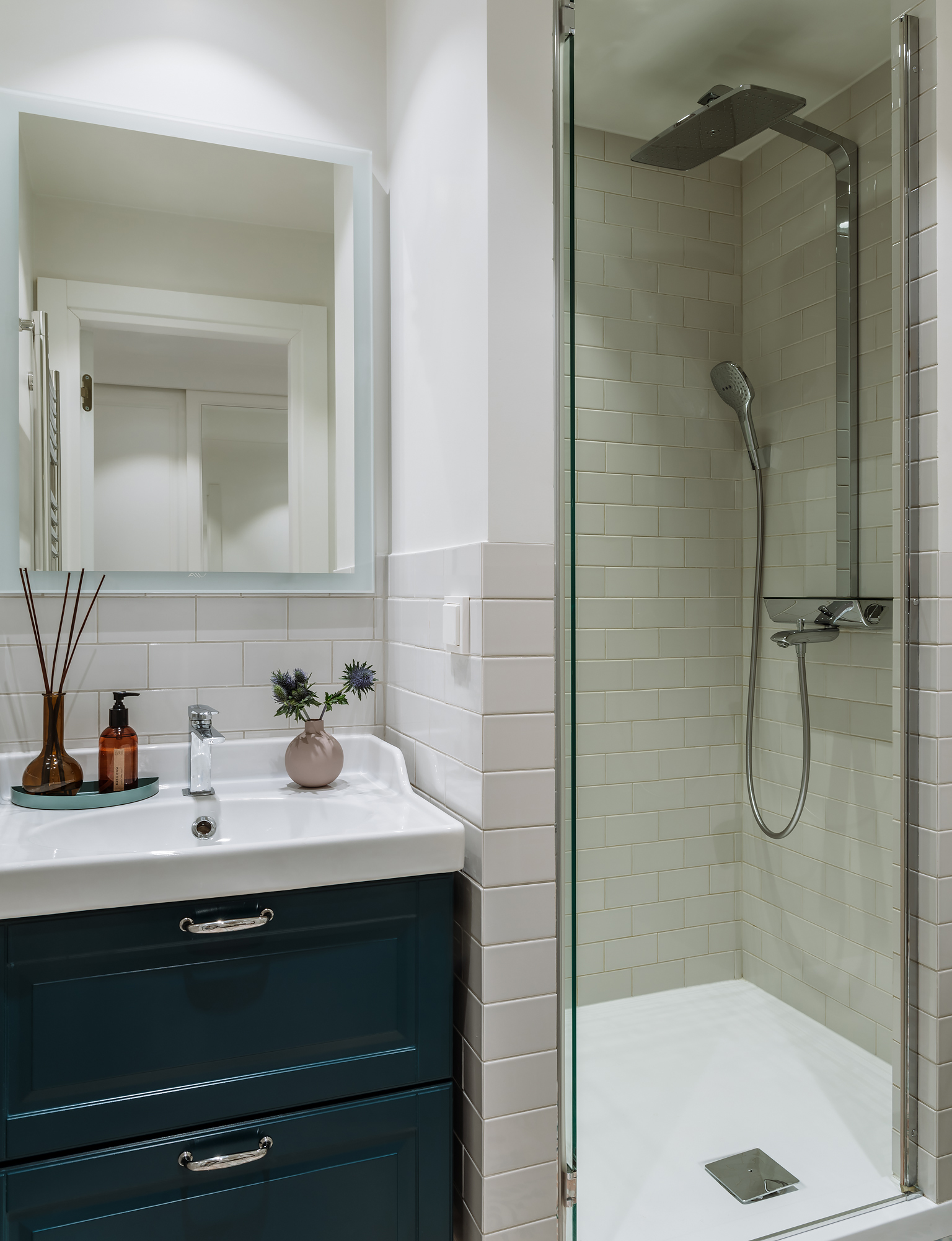 Phòng tắm và nhà vệ sinh nhỏ hẹp nhưng vẫn tinh tế với tủ vanity màu xanh cổ vịt đậm, lọ tinh dầu tỏa hương trên bệ bồn rửa. Riêng buồng tắm vòi sen được phân vùng bằng cửa trượt kính trong suốt.