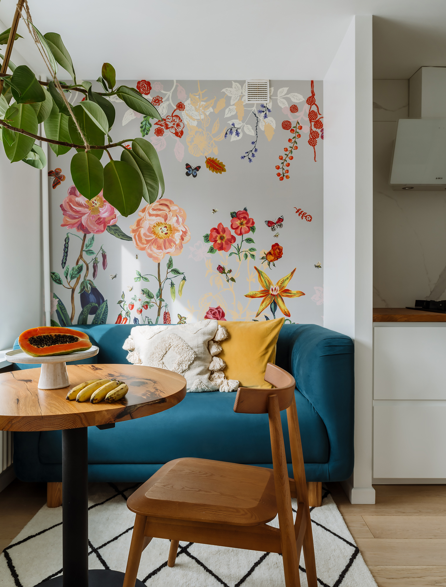 Phòng khách với ghế sofa màu xanh cổ vịt thời trang cùng gối tựa màu kem và vàng mù tạt. Phía sau sofa, giấy dán tường với những bông hoa khoe sắc cho không gian đầy sức sống.