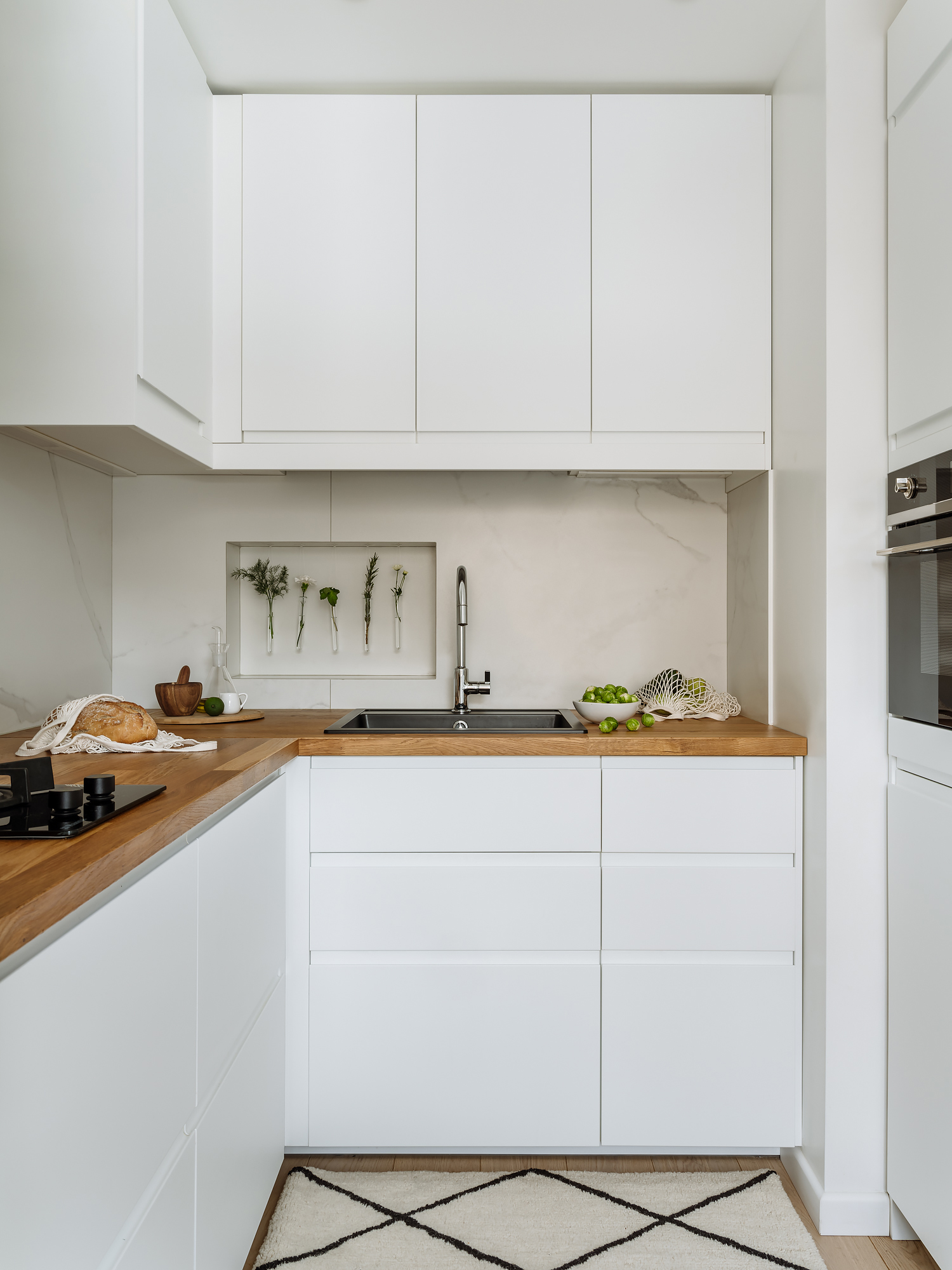 Phòng bếp nhỏ với hệ tủ lưu trữ màu trắng sạch sẽ, tương phản nhẹ nhàng với mặt bàn gỗ ấm áp. Backsplash ốp đá cẩm thạch cho khu vực nấu nướng thêm sang chảnh.