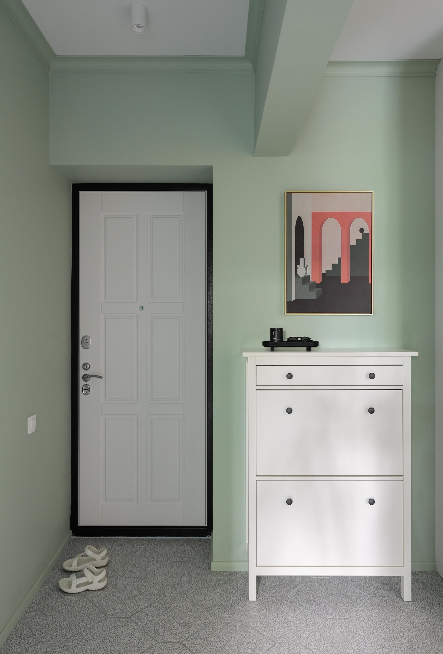 Lối vào căn hộ lựa chọn sắc xanh bạc hà tươi mát cho màu sơn tường, tương phản nhẹ nhàng với cửa ra vào, trần nhà và chiếc tủ lưu trữ đồng màu trắng sạch sẽ.