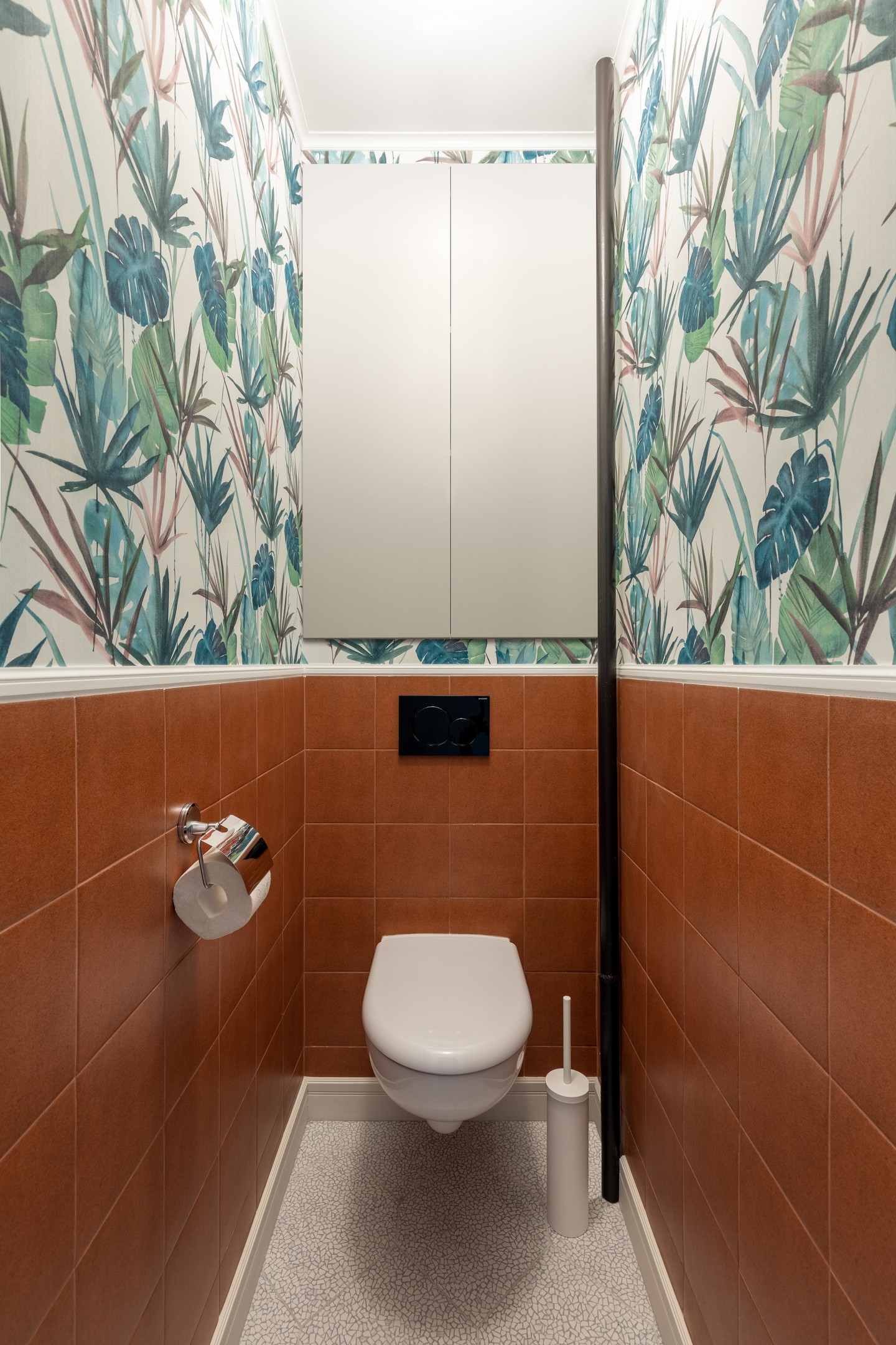 Giấy dán tường tiếp tục phát huy vẻ đẹp trong nhà vệ sinh, với phân nửa bức tường ốp gạch màu đất nung, nửa còn lại là họa tiết tropical sống động. Bồn cầu gắn tường cũng giúp tiết kiệm diện tích và vệ sinh dễ dàng hơn.
