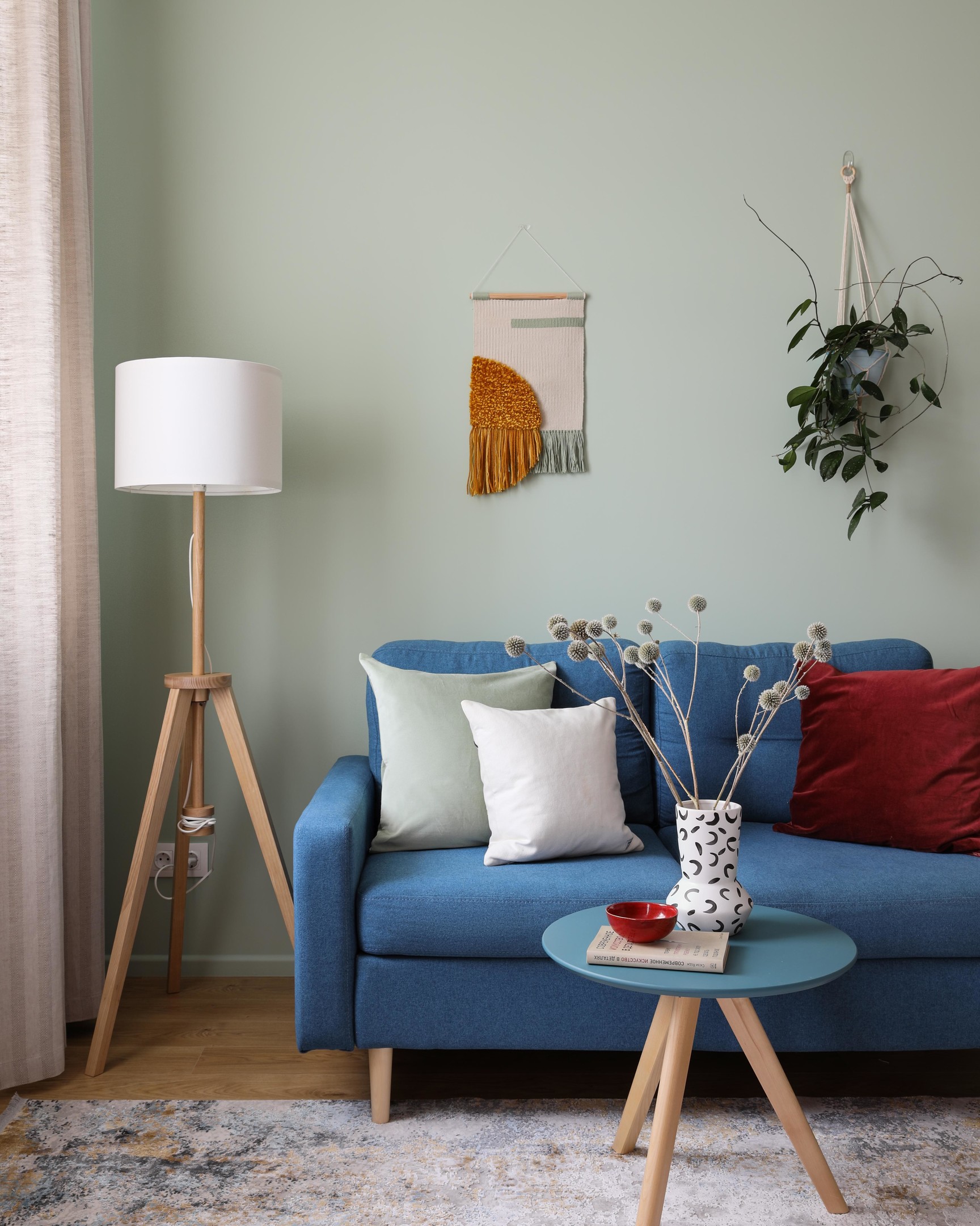 Phòng khách bố trí chiếc ghế sofa màu xanh lam đậm, 'tone sur tone' với bàn nước hình tròn nhỏ nhắn và được phân vùng với góc làm việc bằng tấm thảm trải sàn êm ái.