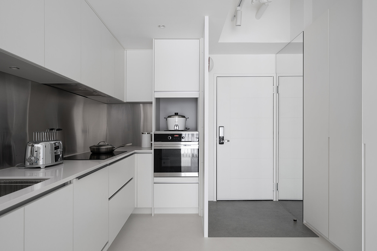 Phòng bếp thiết kế kiểu chữ L, ngay góc phải khu vực lối ra vào nhà. Backsplash ốp kim loại sáng bóng, tạo điểm nhấn giữa hệ thống tủ lưu trữ màu trắng sạch sẽ. Các vật dụng được xếp gọn trong tủ, cho bếp một vẻ ngoài gọn ghẽ.