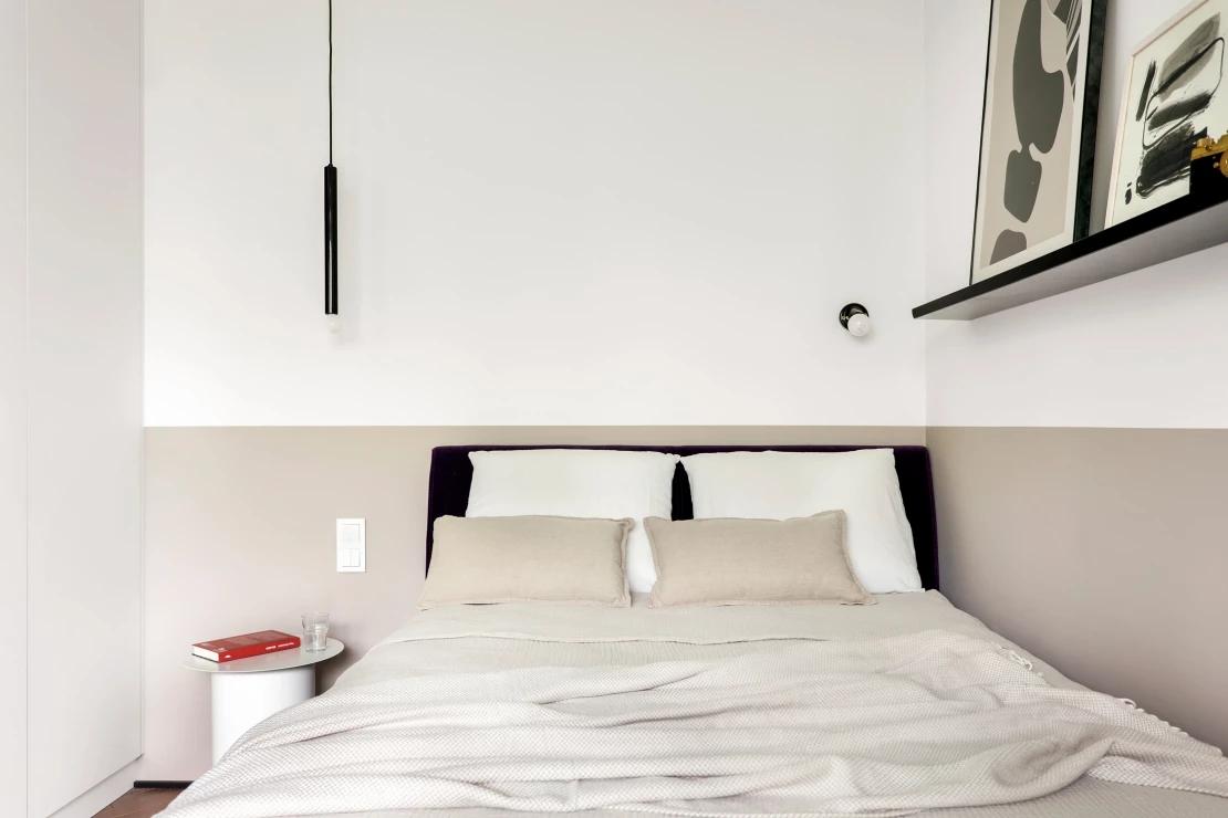 Phòng ngủ thiết kế với tone màu tươi sáng, táp đầu giường có thiết kế tương tự bàn nước tại phòng khách. Riêng đầu giường, đèn thả trần và kệ mở sử dụng gam màu đen để tạo cảm giác nam tính giữa không gian tối giản. 