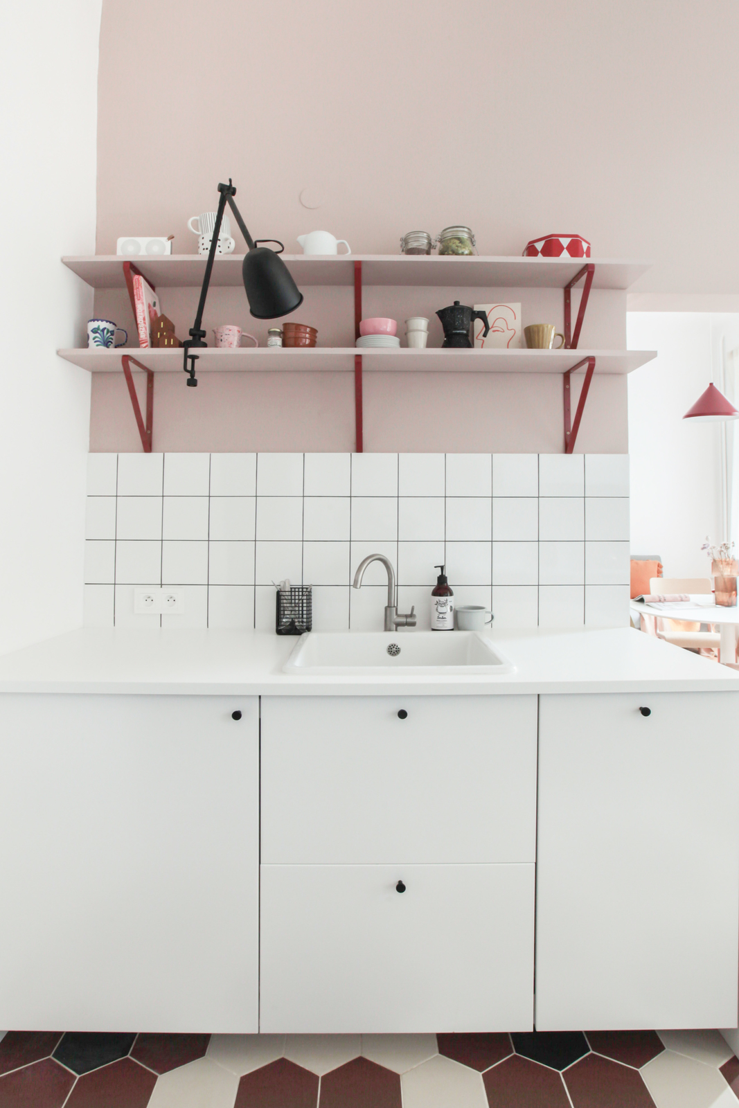 Khu vực bồn rửa chén bát tuy nhỏ nhưng xinh xắn với tone màu trắng và hồng nữ tính, kết hợp backsplash ốp gạch mosaic trắng và hệ thống kệ mở phía trên cho cái nhìn gọn gàng, sạch sẽ.
