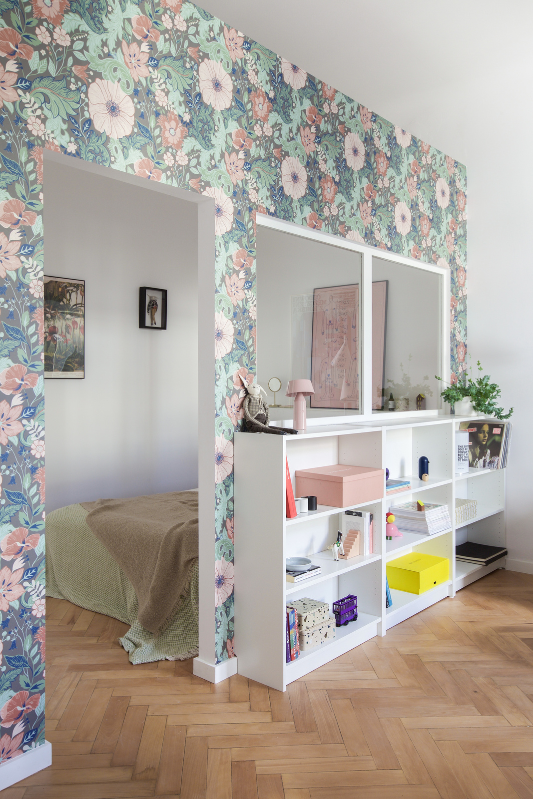 Góc phải phòng khách là không gian dành cho kệ lưu trữ gọn gàng và phòng ngủ xinh xắn được tô điểm bằng giấy dán tường. Và dĩ nhiên, vẫn là hình ảnh của những bông hoa đang khoe sắc trên nền là những tán lá xanh tươi.