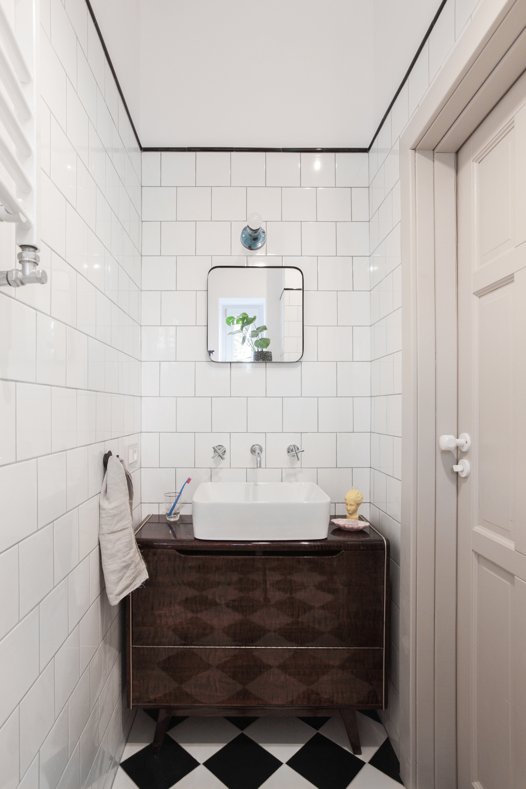 Phòng tắm sử dụng gạch trắng ốp tường và gương soi hình vuông tạo cảm giác rộng rãi hơn so với diện tích thật. Sàn ốp gạch trắng - đen cổ điển, cả chiếc tủ vanity cũng theo phong cách hoài cổ, bề mặt sáng bóng phản chiếu hình ảnh phòng tắm nhỏ xinh.