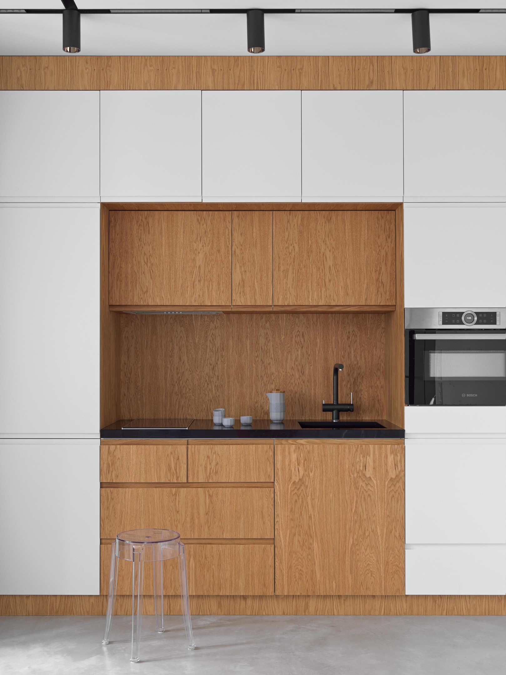 Phòng bếp kiểu chữ I tạo lối đi thông thoáng, bao quanh bếp nấu là hệ thống tủ lưu trữ ngăn nắp với sự tương phản giữa tone màu trắng và gỗ mộc mạc.