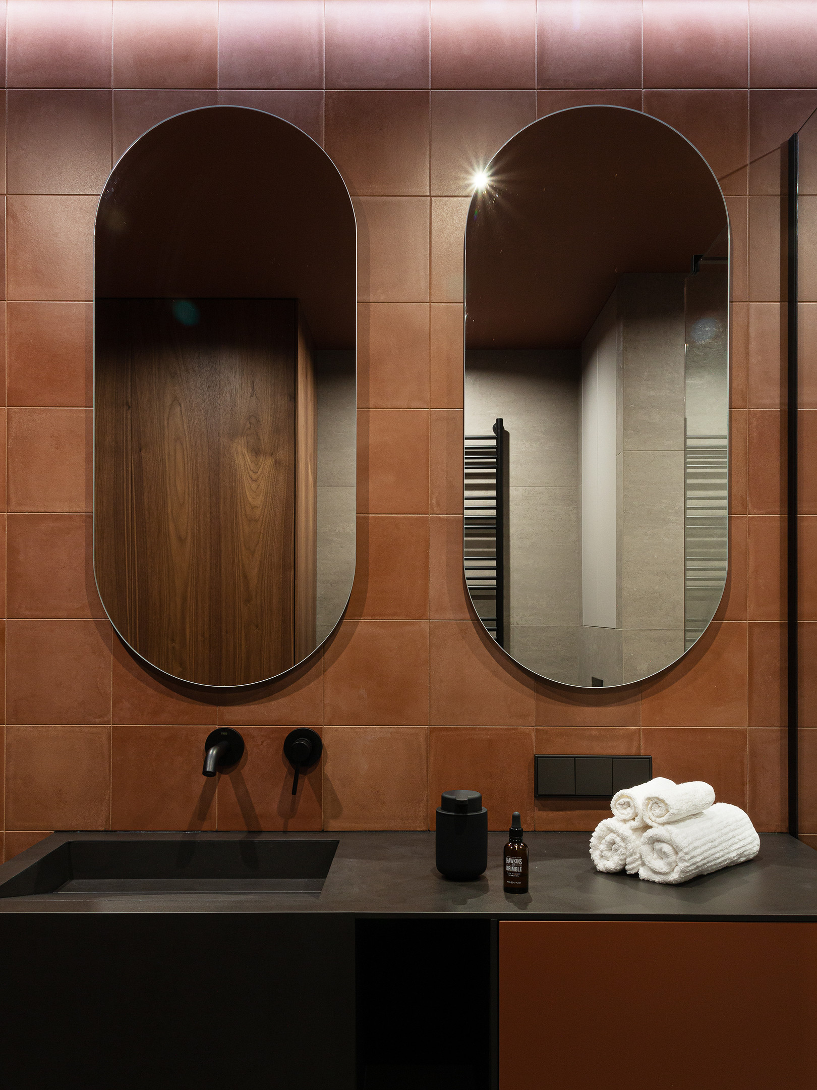 Riêng khu vực bồn rửa với gam màu đen vững chãi, phía trên tường lắp đặt đến 2 tấm gương hình oval nhằm góp phần nhân đôi hình ảnh và ánh sáng cho phòng tắm nhỏ rộng rãi, sáng sủa hơn.