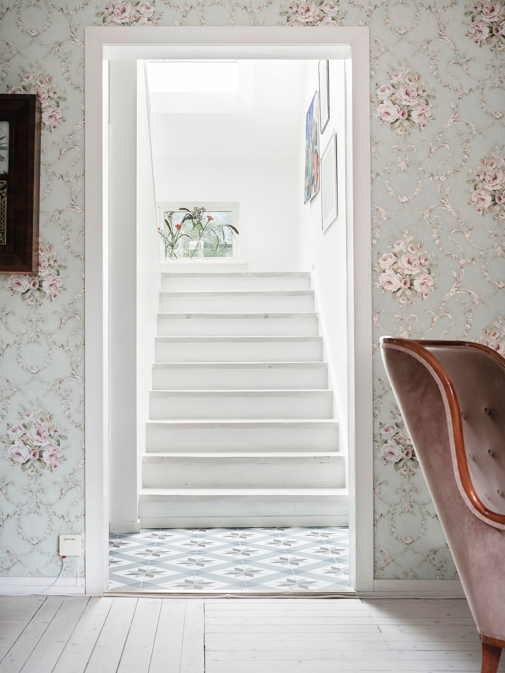 Cầu thang dẫn lối lên tầng gác mái được trang trí với những bức tranh treo tường cùng vài lọ hoa thủy tinh đẹp mắt trên bệ cửa sổ.