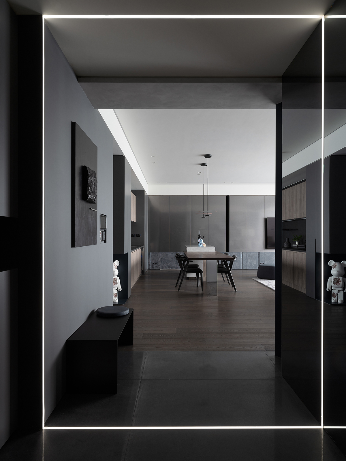 Lối vào thể hiện ngay phong cách thiết kế của căn hộ, với sàn nhà lát đá xám đậm, băng ghế nghỉ chân màu đen tuyền cùng tấm gương màu xám tích hợp đèn chiếu sáng cho cảm giác không gian như rộng ra gấp đôi.