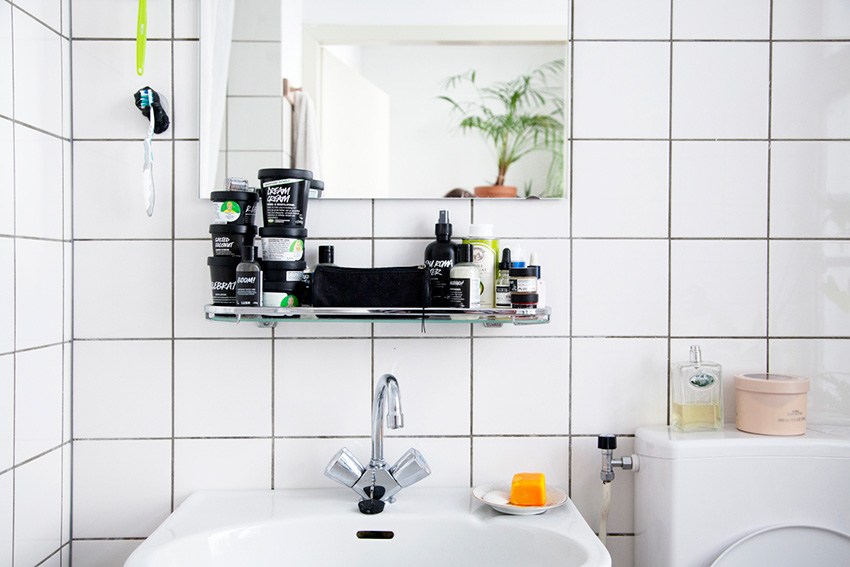 Phòng tắm ốp gạch mosaic vuông với gam màu trắng cho cảm giác sạch sẽ. Kệ đựng mỹ phẩm bằng kính lắp đặt ngay phía trên bồn rửa giúp tiết kiệm diện tích tối ưu.