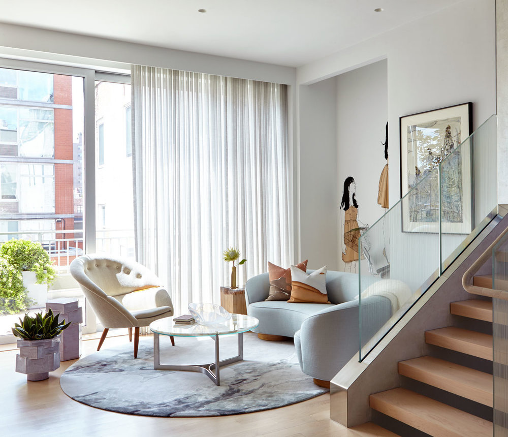 Phòng khách trong căn hộ thông tầng với chiếc ghế sofa hình bán nguyệt màu xanh lam nhạt, kết nối với ghế bành màu trắng kem trông vô cùng ngọt ngào, xinh xắn.
