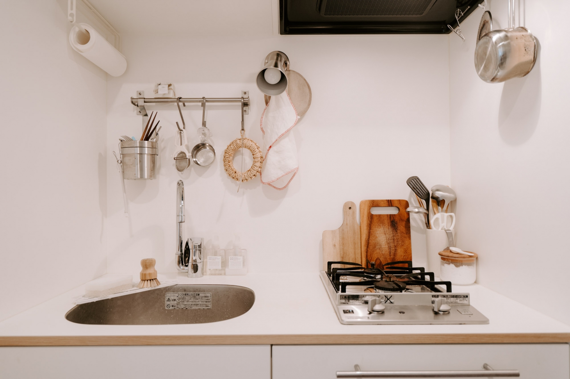 Khu vực nấu nướng nhỏ gọn với một chiếc bếp đơn và bồn rửa, kết hợp nhiều móc treo gắn tường để lưu trữ dụng cụ nấu nướng, khăn lau, cuộn giấy ăn,...