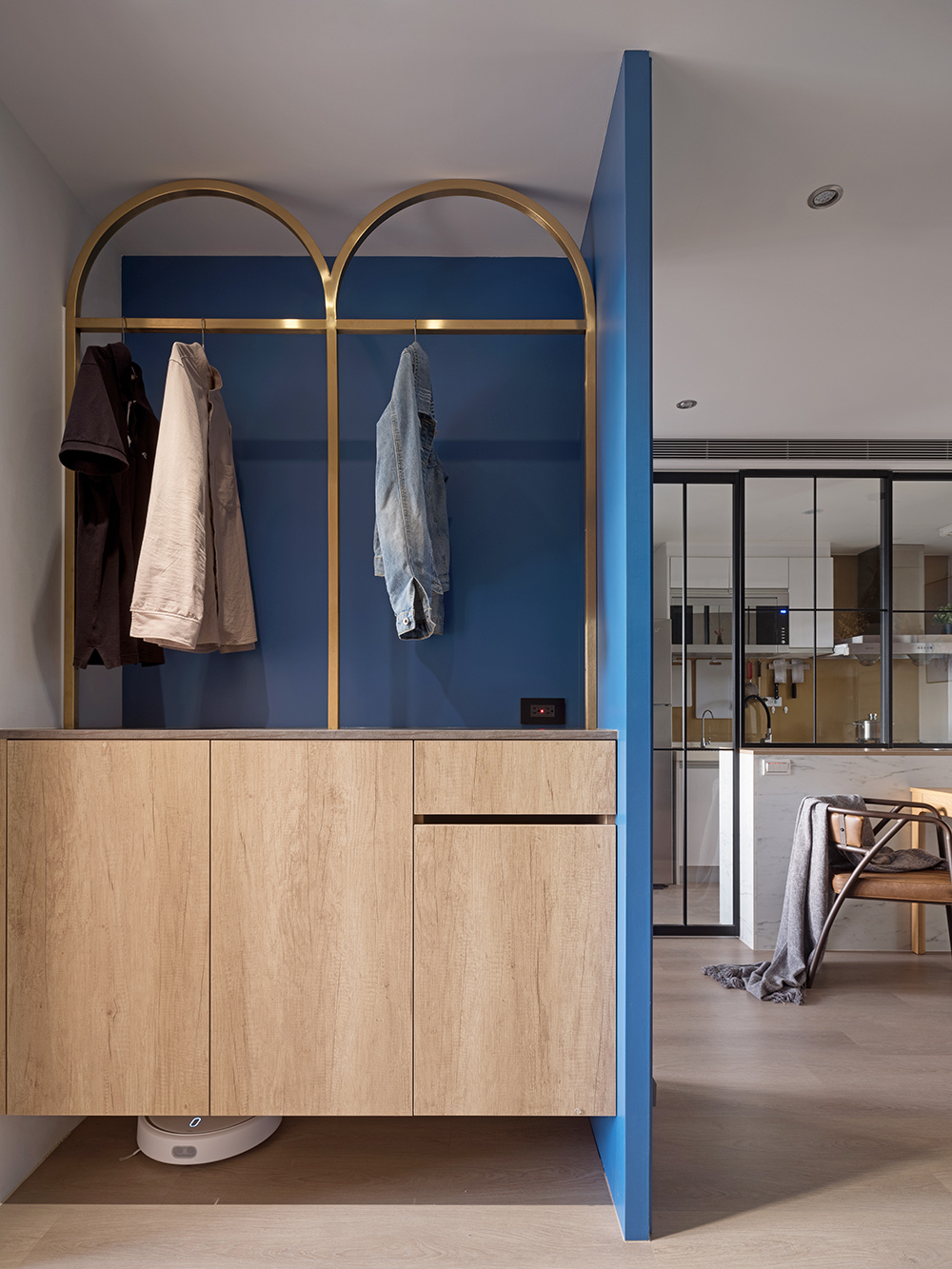 Lối vào căn hộ bắt mắt với khu vực lưu trữ được bao quanh bởi gam màu xanh coban kết hợp tủ gỗ và khung treo áo khoác bằng kim loại mạ vàng đồng kiểu mái vòm ấn tượng.