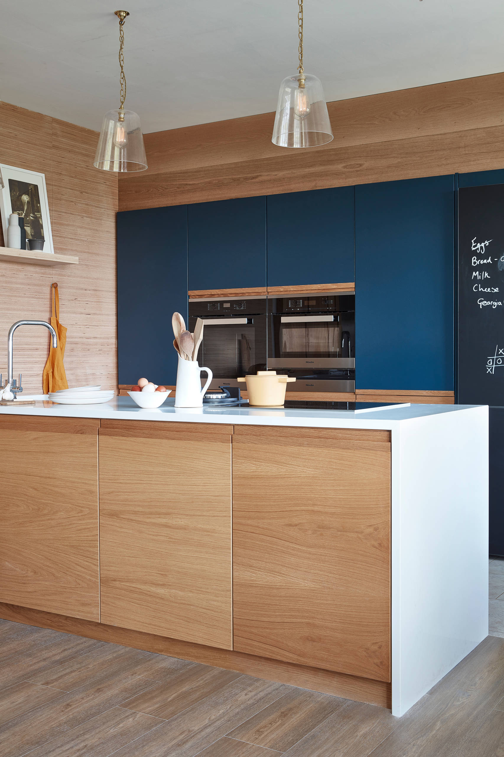 Chúng tôi yêu vẻ đẹp vừa ấm áp vừa vững chãi của căn bếp nhỏ với điểm nhấn là tủ bếp màu xanh lam đậm, bao bọc xung quanh là nội thất gỗ mộc mạc. Nếu tinh ý, bạn sẽ nhận ra bức tường sử dụng giấy dán, còn đảo bếp mới ốp gỗ thật.