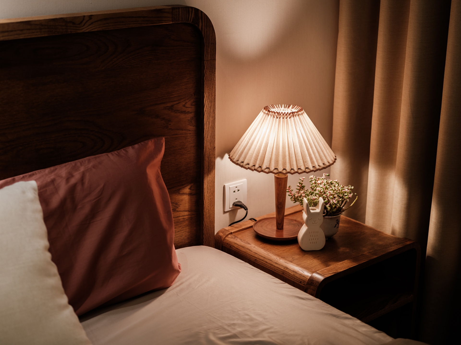 Táp đầu giường bằng gỗ nhỏ gọn với chiếc đèn ngủ phong cách cổ điển, lọ hoa trang trí và đặc biệt là một chú thỏ trắng dễ thương.