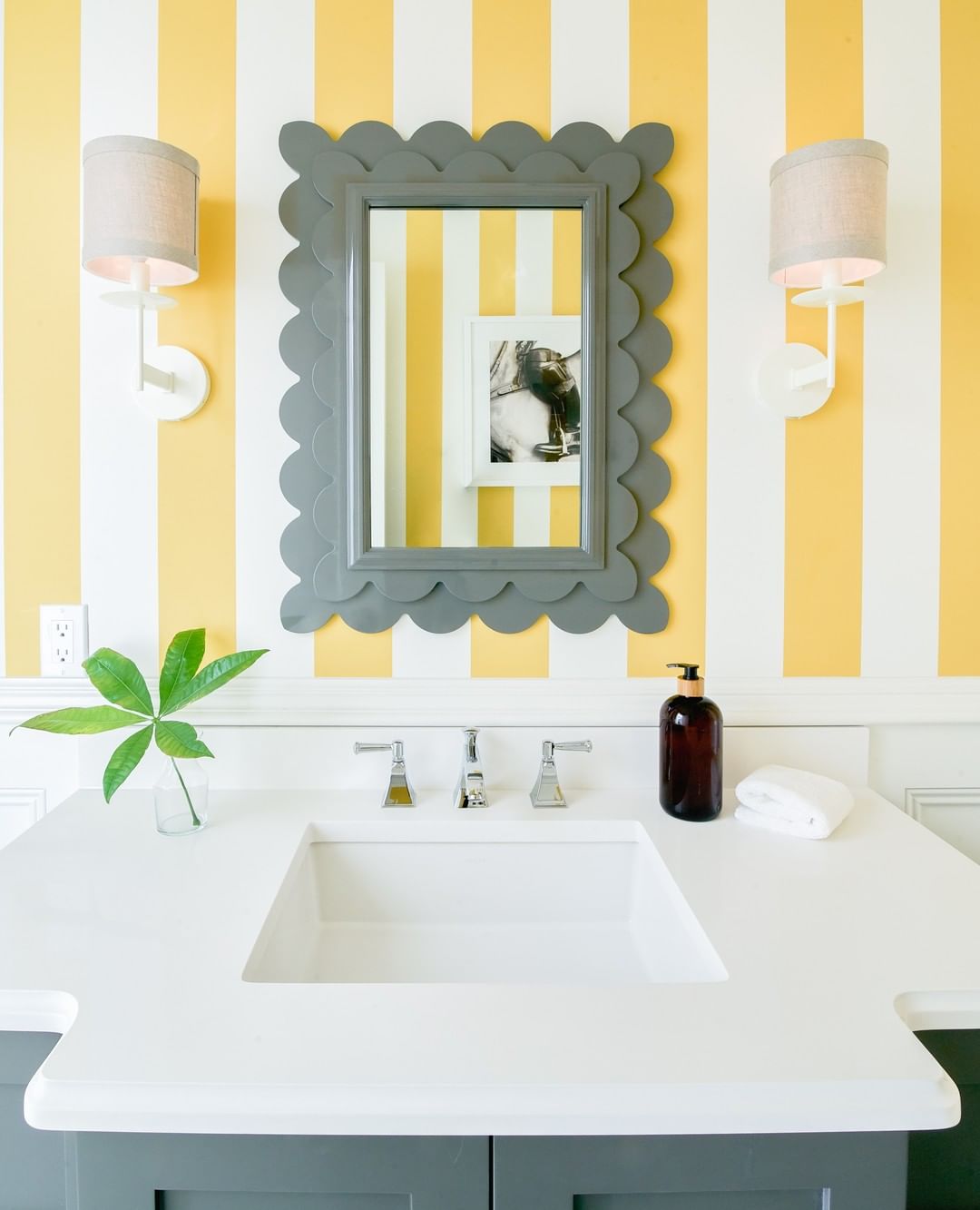 Họa tiết kẻ sọc vàng - trắng của giấy dán tường kết hợp thiết kế xếp lớp kiểu vảy cá cho khung gương giúp khu vực bồn rửa bắt mắt hơn. Mẫu giấy dán tường này được sử dụng cho toàn bộ phòng tắm nhưng không hề “chói lóa”.