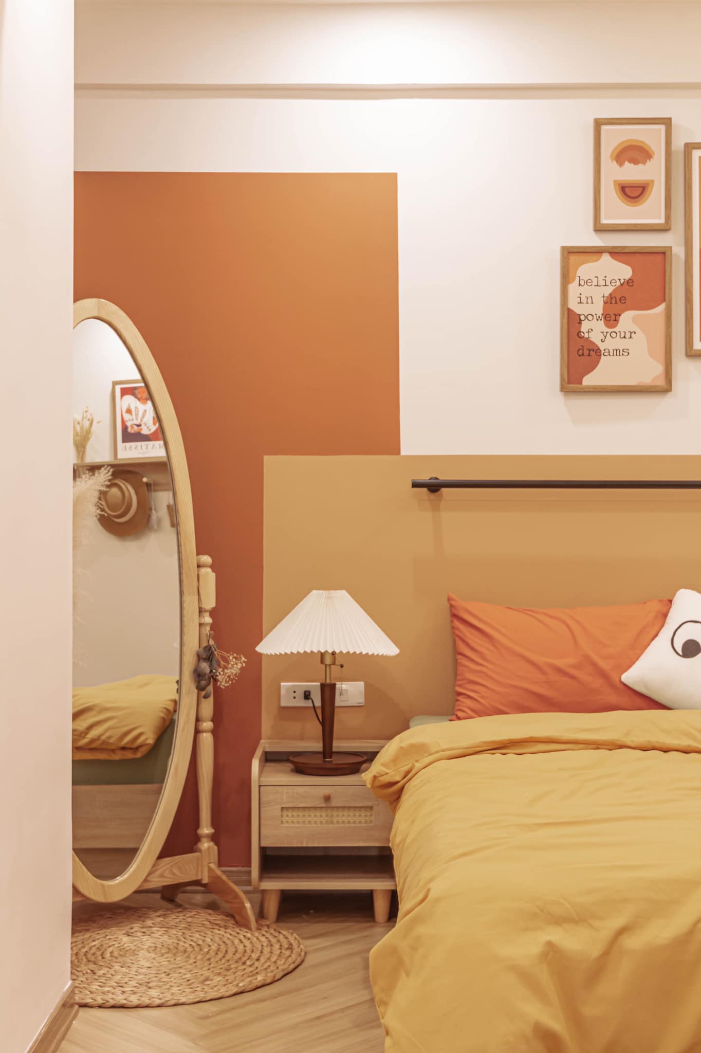 Phòng ngủ của cặp đôi được thiết kế ngọt ngào với tone màu cam, vàng mù tạt và màu be êm ái. Tấm gương hình oval đặt trên tấm thảm lục bình vừa duyên dáng vừa 'cơi nới' không gian bằng thị giác.