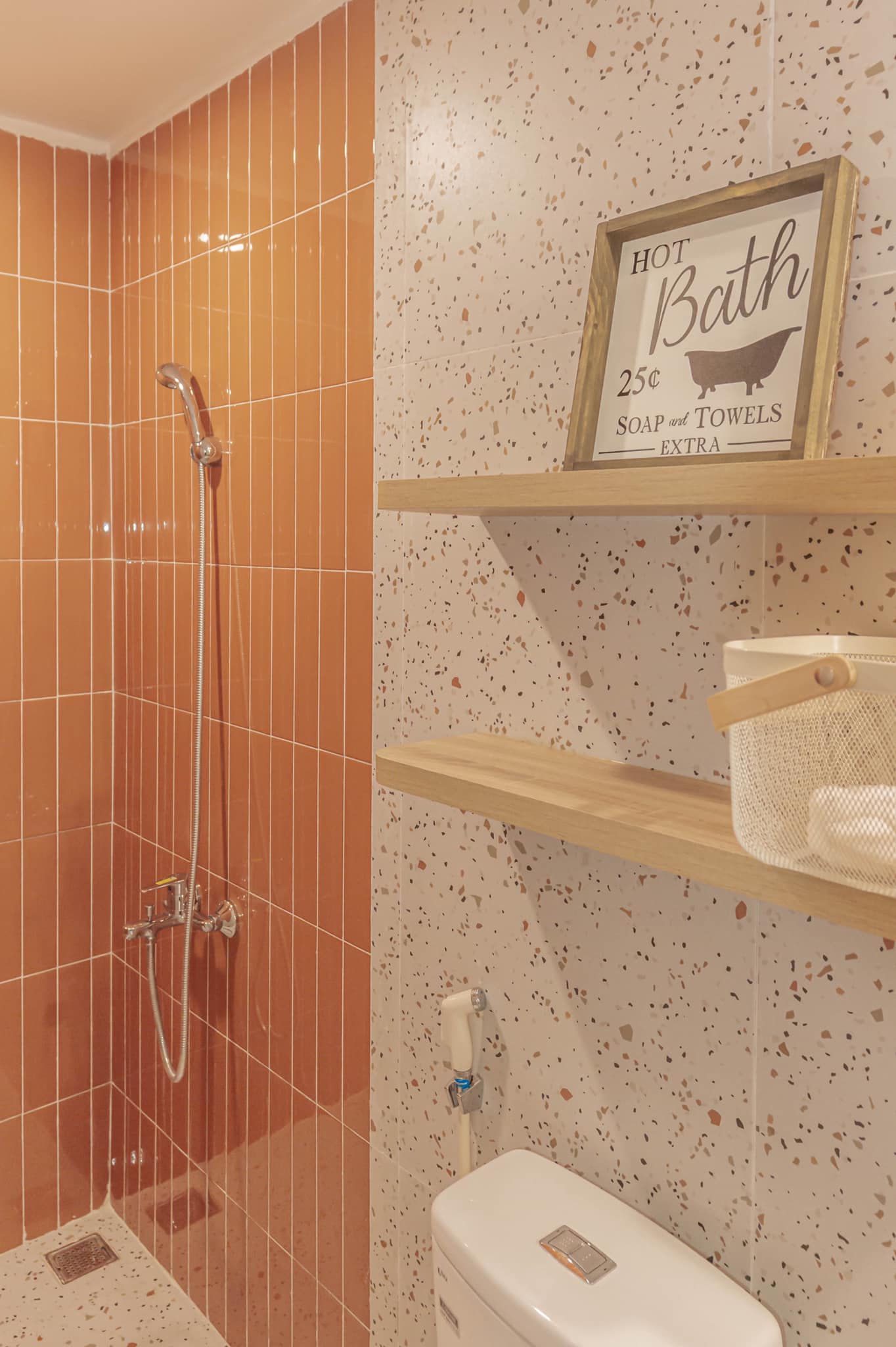 Phòng tắm thứ hai sử dụng gạch ốp tường màu cam để phân vùng buồng tắm đứng và toilet. Kệ mở được tận dụng để lưu trữ gọn gàng hơn và không tốn diện tích sàn.