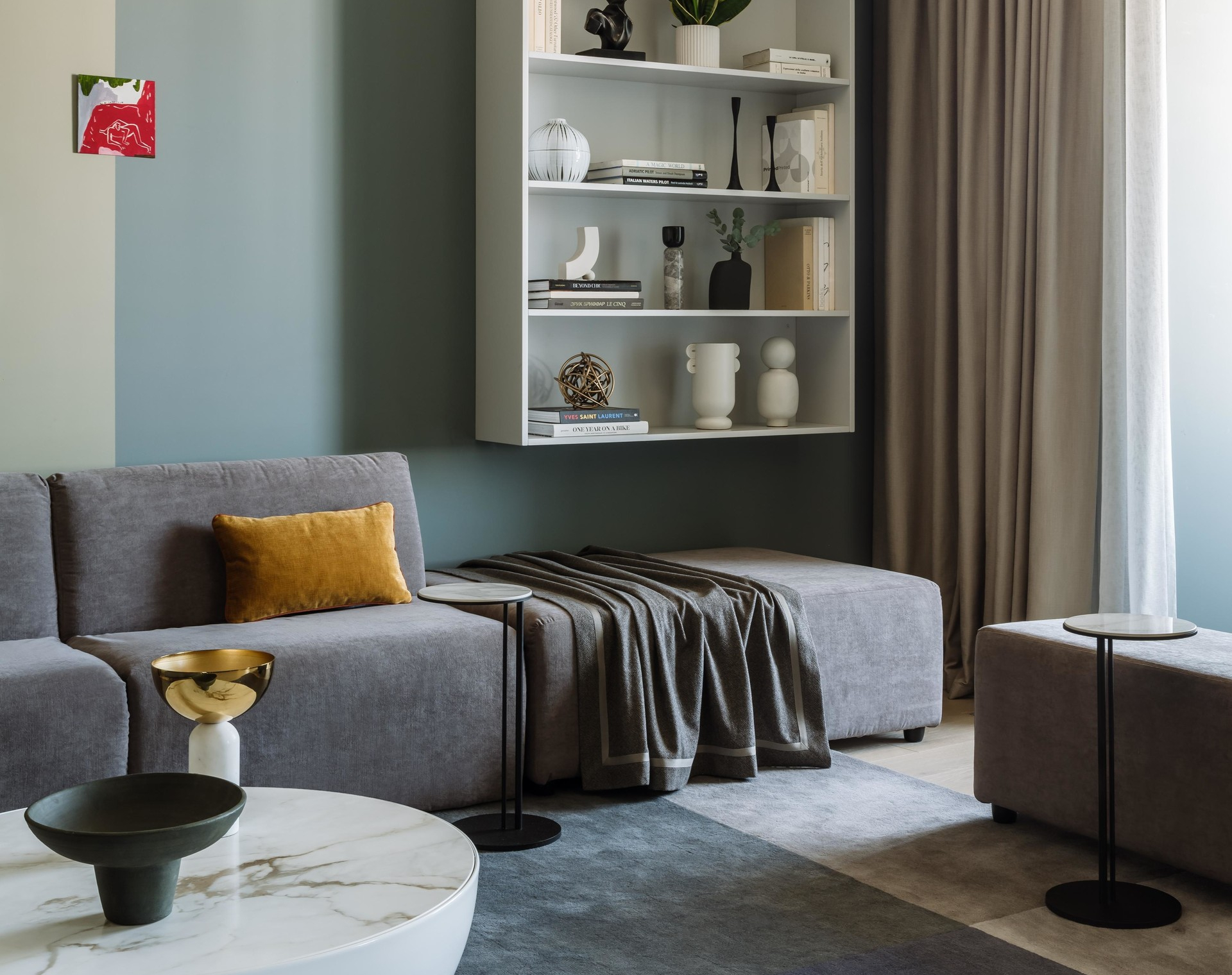 Sofa kiểu module linh hoạt hoàn toàn có thể trở thành chỗ nằm ngủ thoải mái khi cần. Phía trên tường, NTK sử dụng màu sơn xanh pastel và trắng xám để phân vùng , tạo điểm nhấn cho kệ trang trí gắn tường.