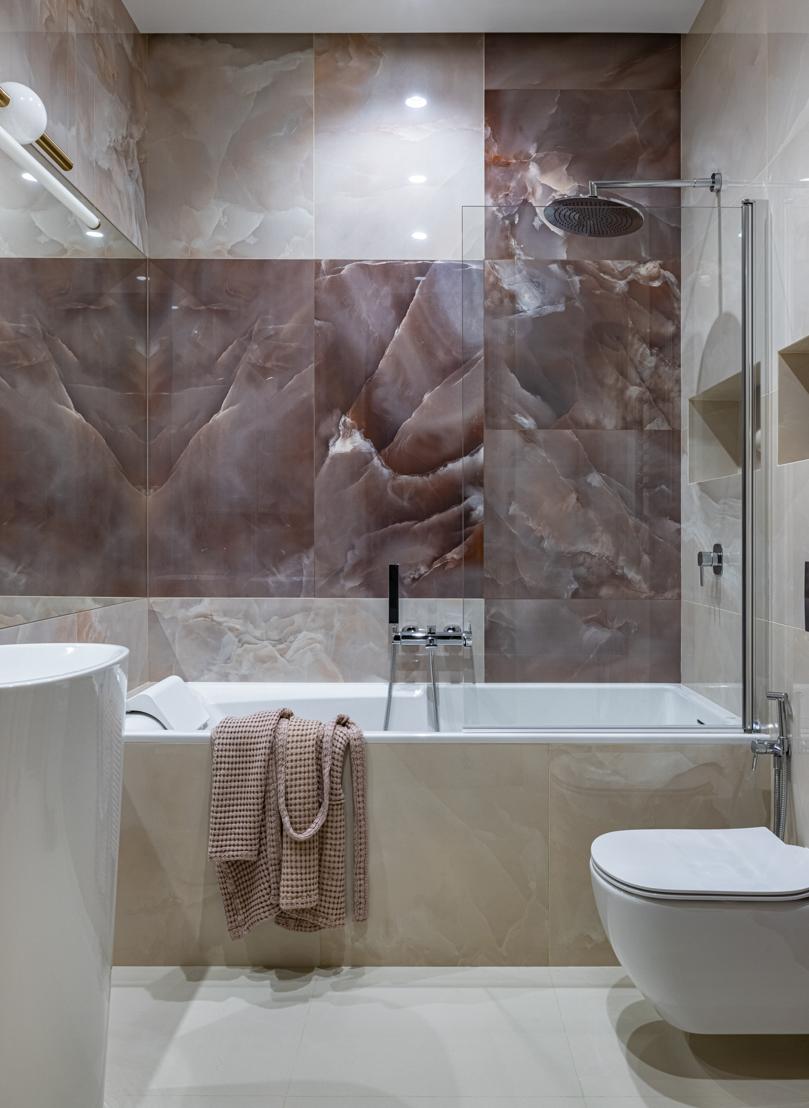 Phòng tắm và nhà vệ sinh siêu sang chảnh với bức tường ốp đá tự nhiên kết hợp hệ thống đèn chiếu sáng long lanh như một tác phẩm nghệ thuật. Toilet gắn tường hiện đại, phân vùng với bồn tắm nằm bằng vách ngăn kính trong suốt.