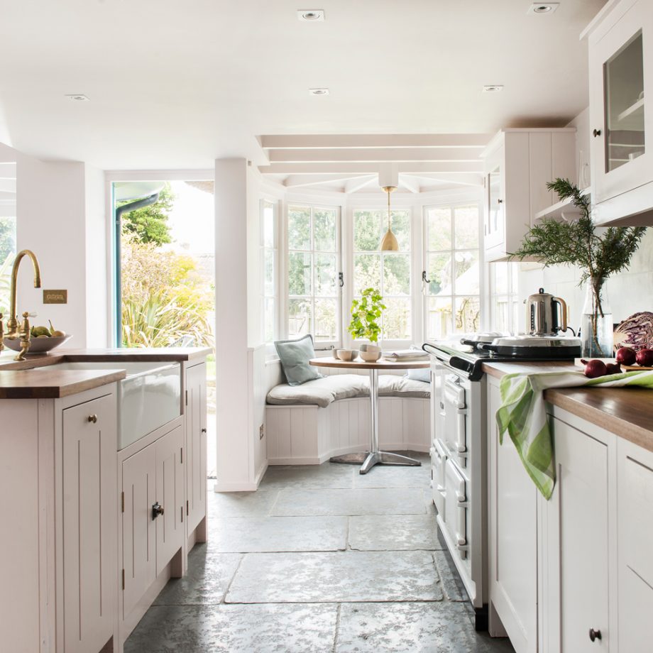 Phòng bếp với sàn nhà lát đá thô mộc, gam màu trắng chủ đạo kết hợp mặt bàn gỗ cho cái nhìn tương phản nhẹ nhàng. Khu vực cửa sổ lồi được tận dụng để thiết lập góc ăn uống lãng mạn nhìn ra khu vườn ngay trong phòng bếp.
