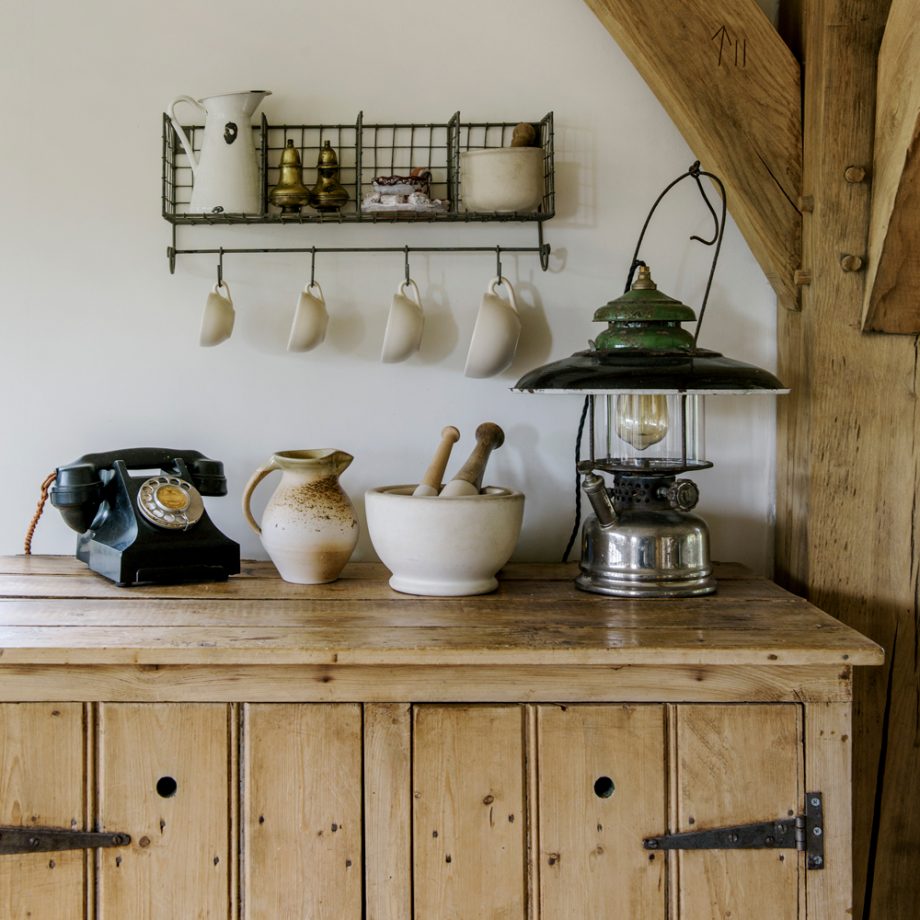 Mọi ngóc ngách của căn bếp đều toát lên vẻ đẹp yên bình đúng “chất” đồng quê. Vật liệu gỗ thô mộc từ bàn bếp đến cột nhà, chiếc đèn bão và điện thoại cũ xưa. Thêm vào những món đồ bằng gốm sứ có thiết kế nhẹ nhàng tinh tế.