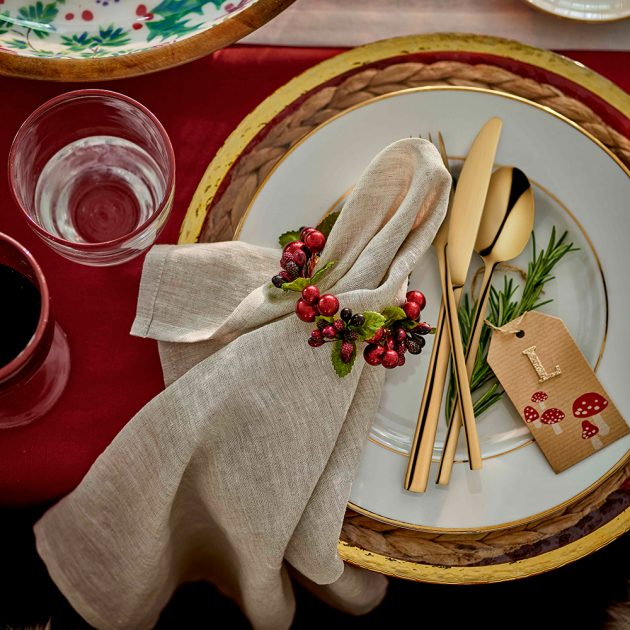 Đĩa ăn sang trọng với những dụng cụ ăn uống mạ vàng đồng lấp láp, thêm vào chiếc khăn ăn được tô điểm bằng vòng nguyệt quế mini với những quả đỏ nổi bật.