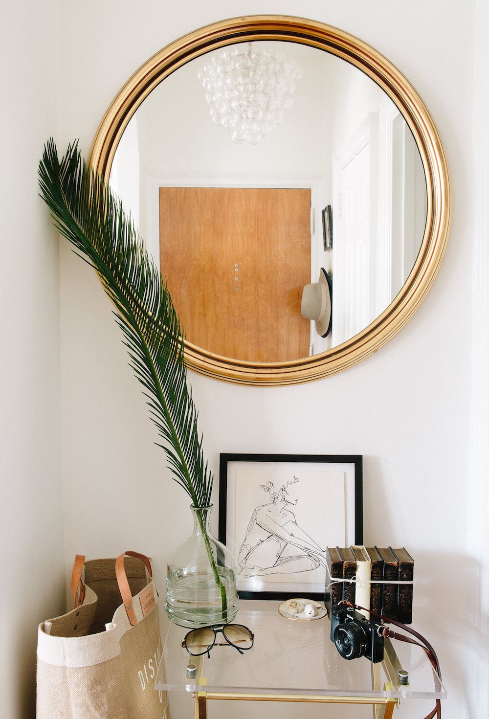 Lối vào căn hộ xinh xắn, với chiếc đèn chùm bong bóng thủy tinh phản chiếu qua tấm gương tròn treo tường. Trên chiếc bàn nhỏ đặt vài phụ kiện, món đồ nhỏ xinh và nhánh lá mềm mại.